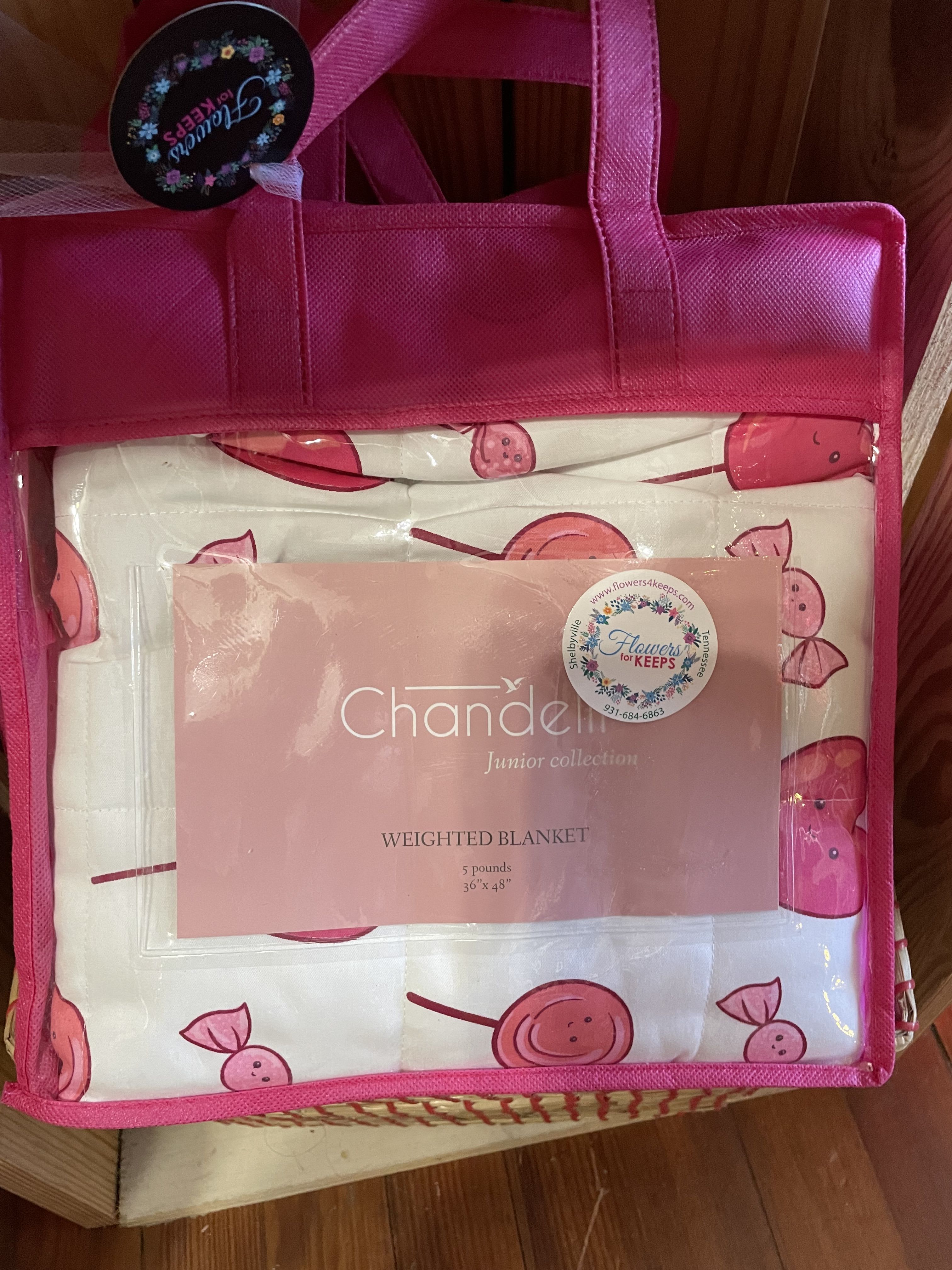 Pink tote bag holding a packaged weighted blanket with cherry print