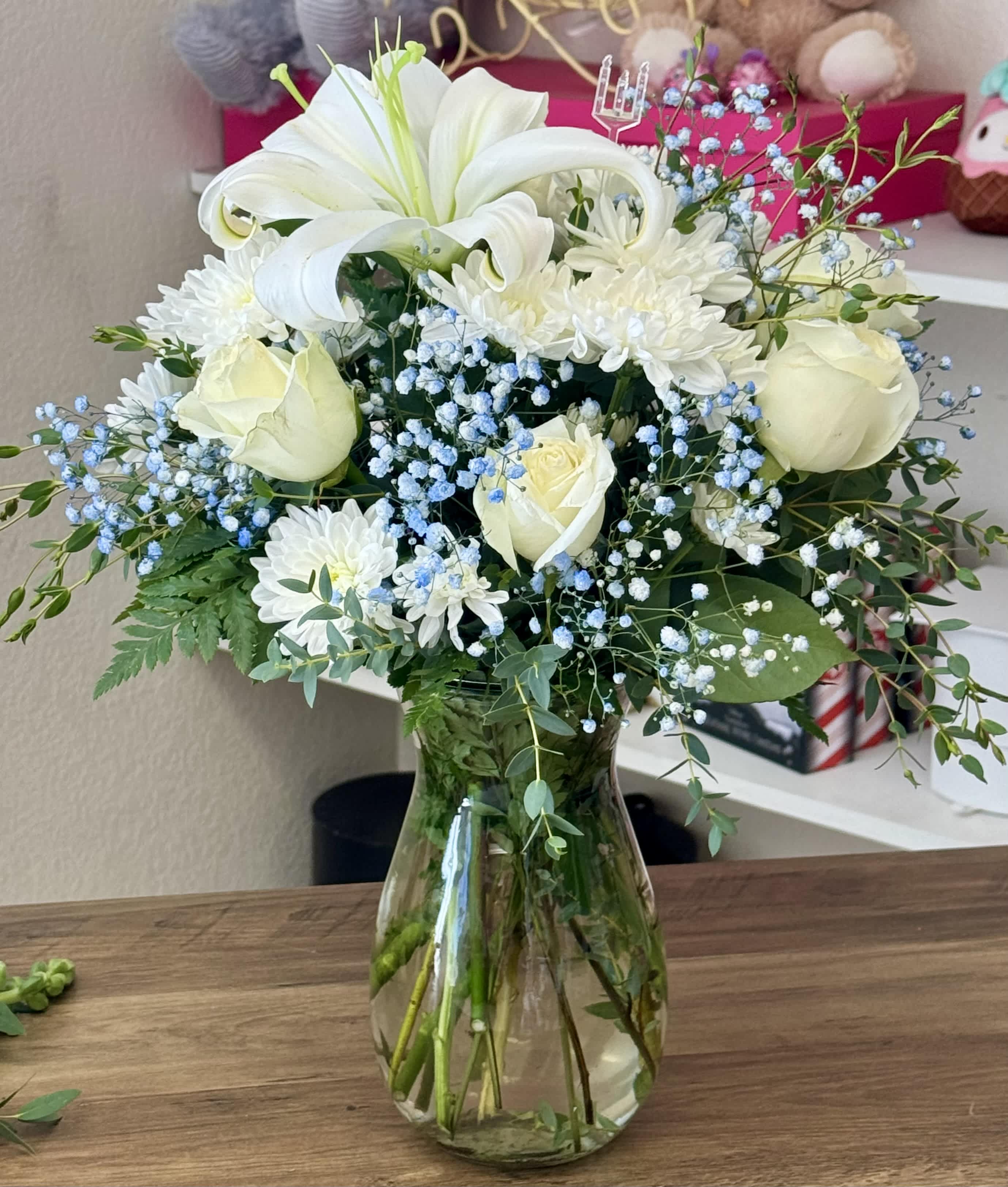 White lilies, roses, and daisies in a glass vase with blue baby's breath