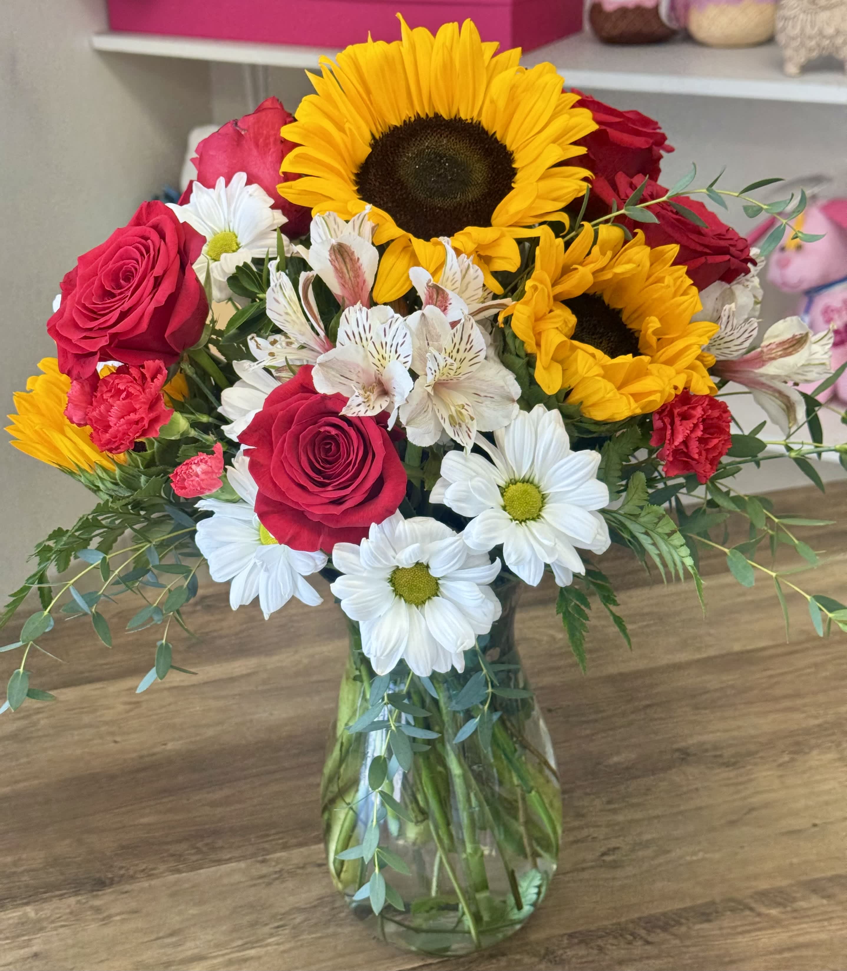 Bouquet of sunflowers, red roses, and white daisies in a glass vase