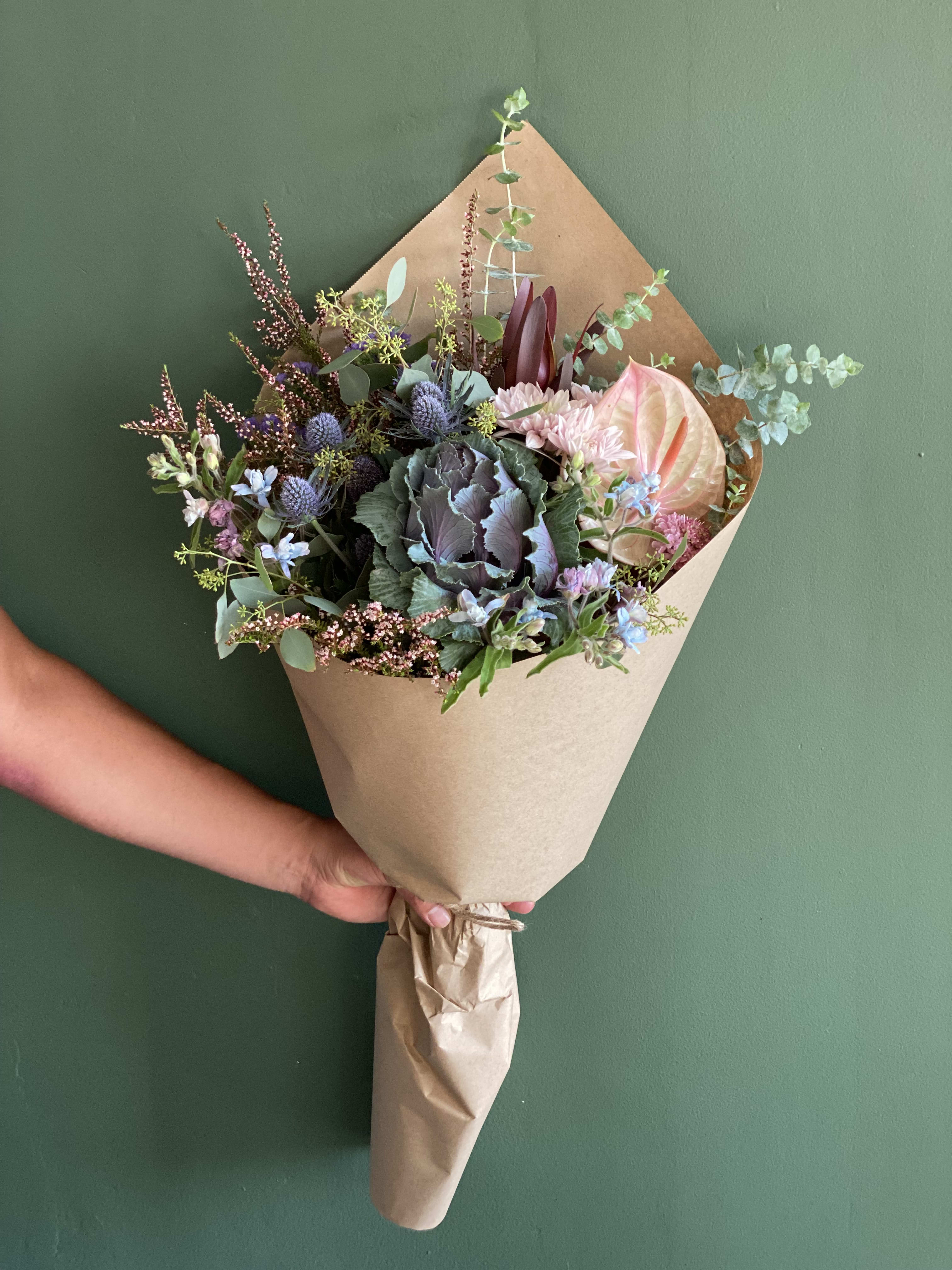 Handheld bouquet with anthurium, thistle, and mixed blooms in kraft paper