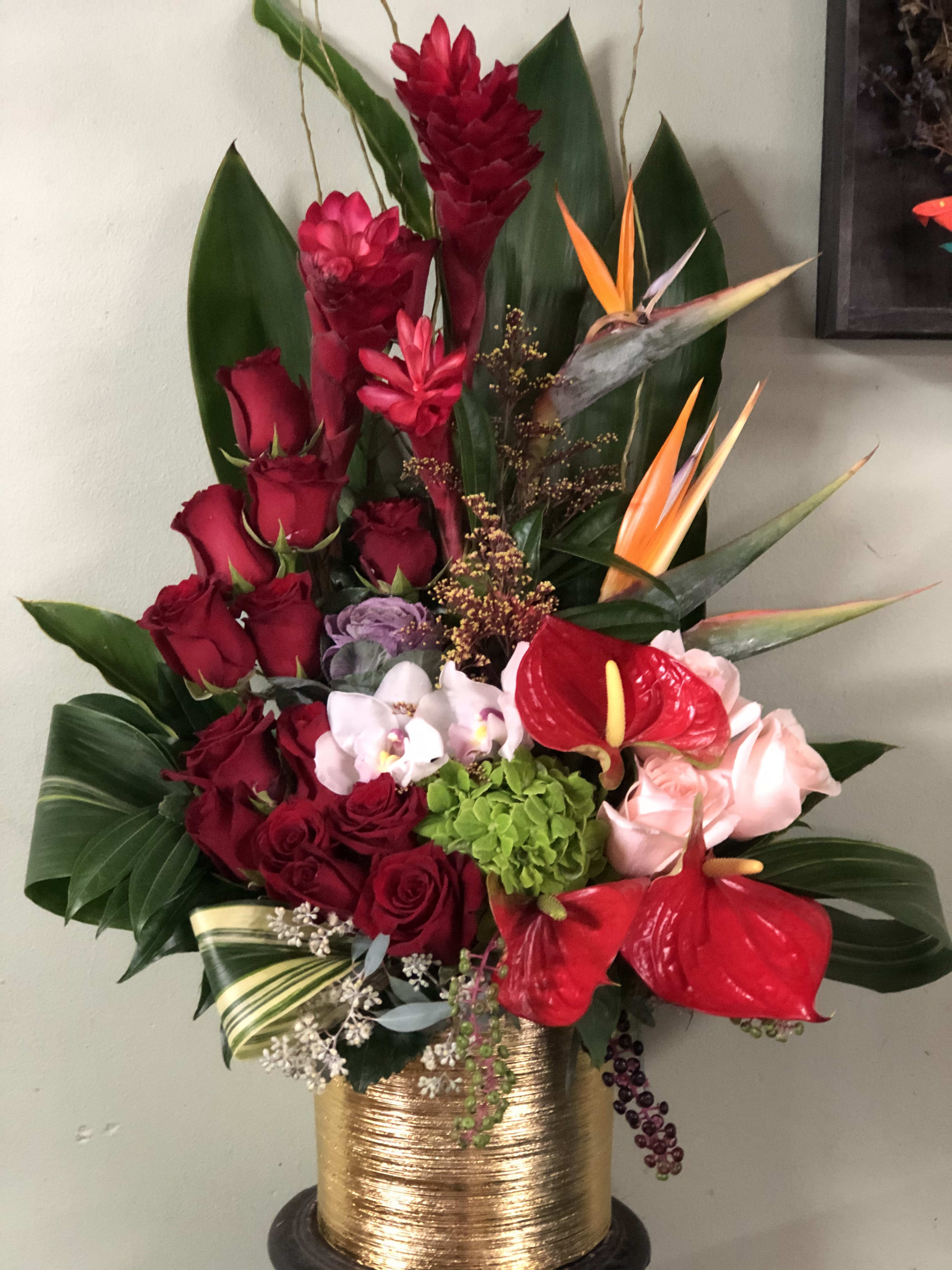 Tall tropical bouquet with red roses, anthuriums, and orchids in a gold vase