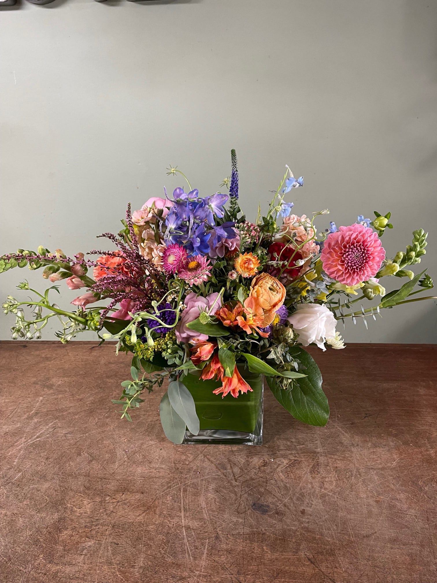Mixed bouquet in a square glass vase with pink, purple, orange, and white flowers.