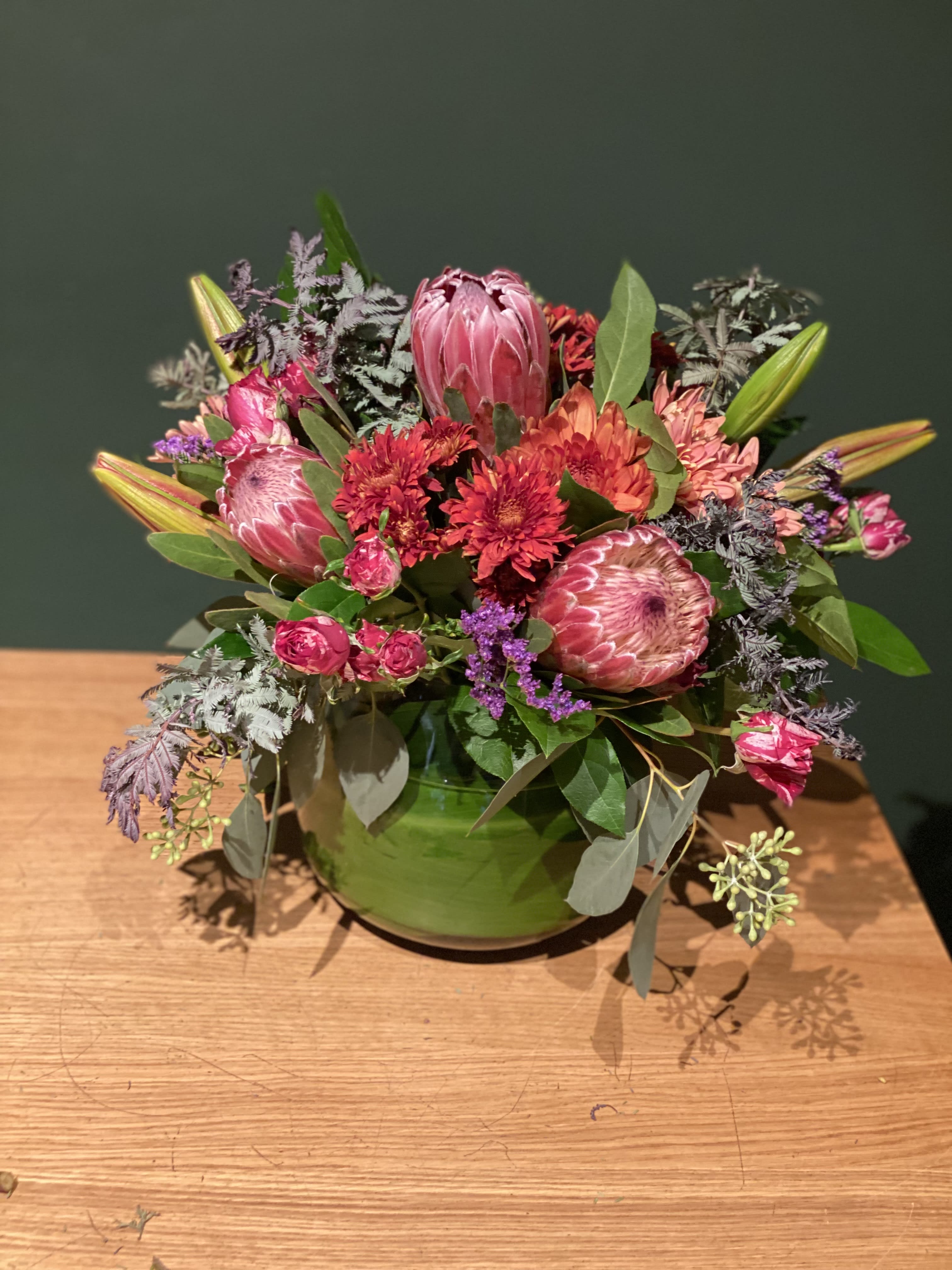 Pink and red mixed flower arrangement in a green bowl vase