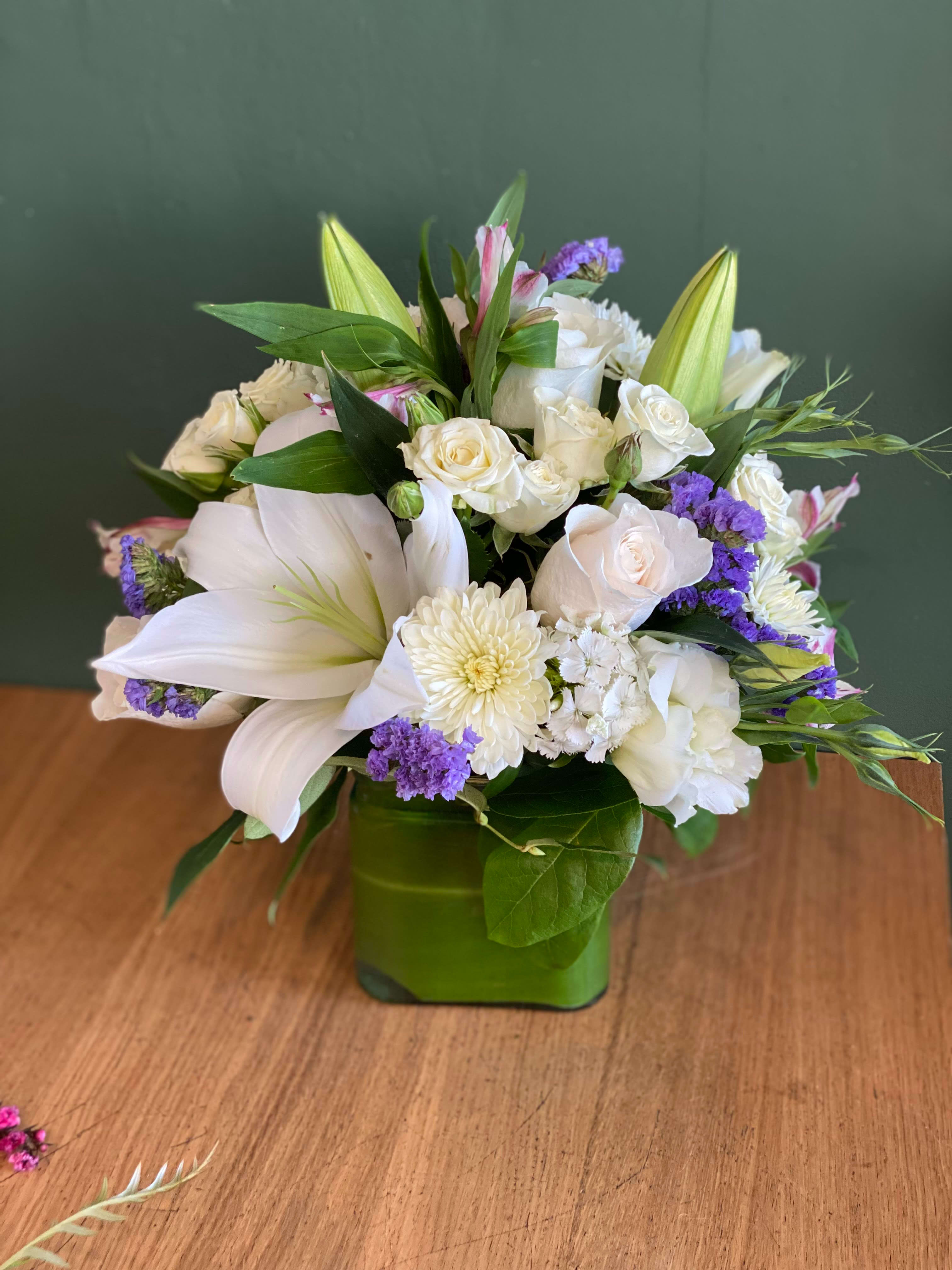 White floral arrangement in a green square vase with purple accents