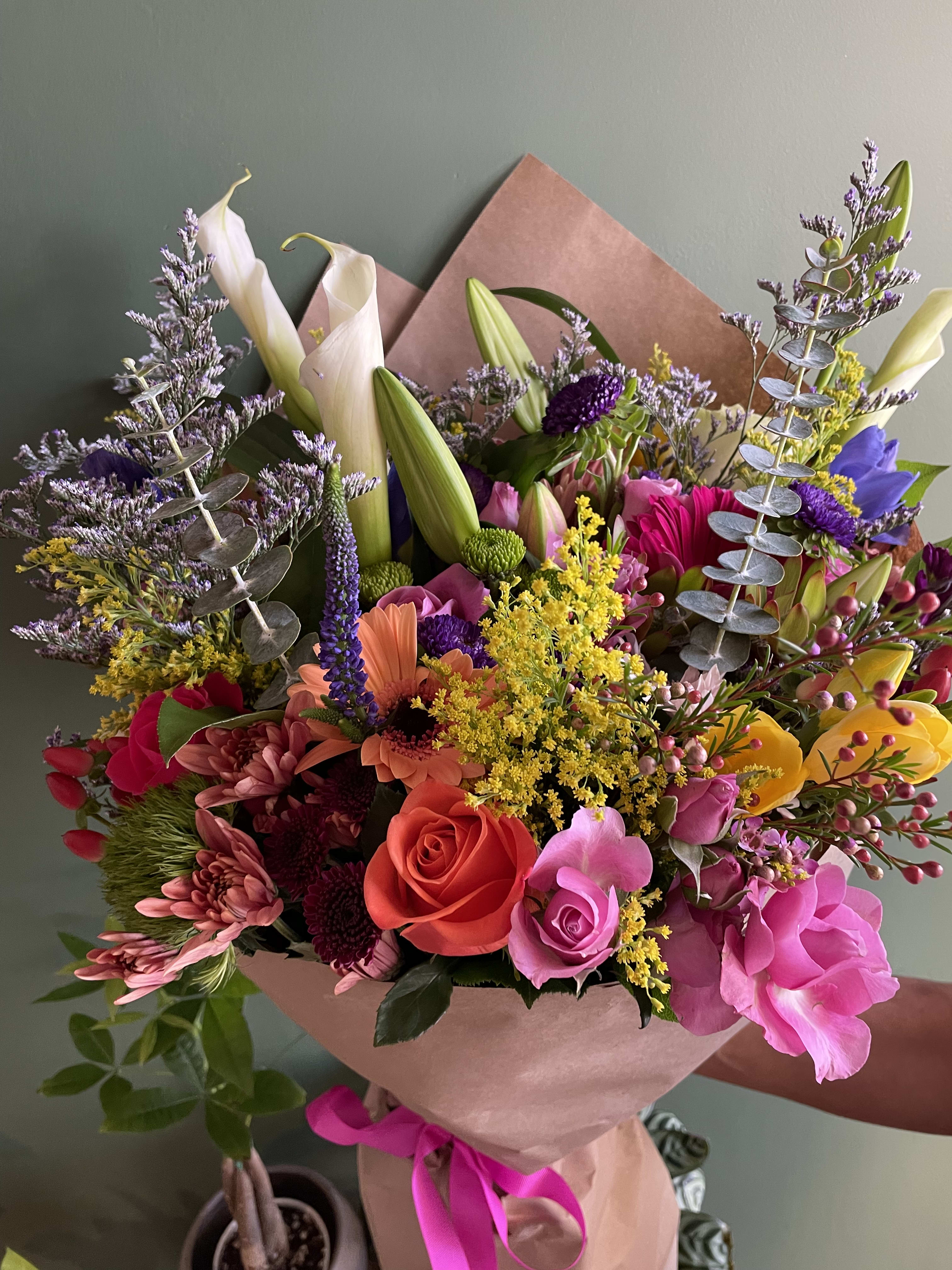 Colorful bouquet with roses, lilies, and mixed blooms wrapped in pink paper