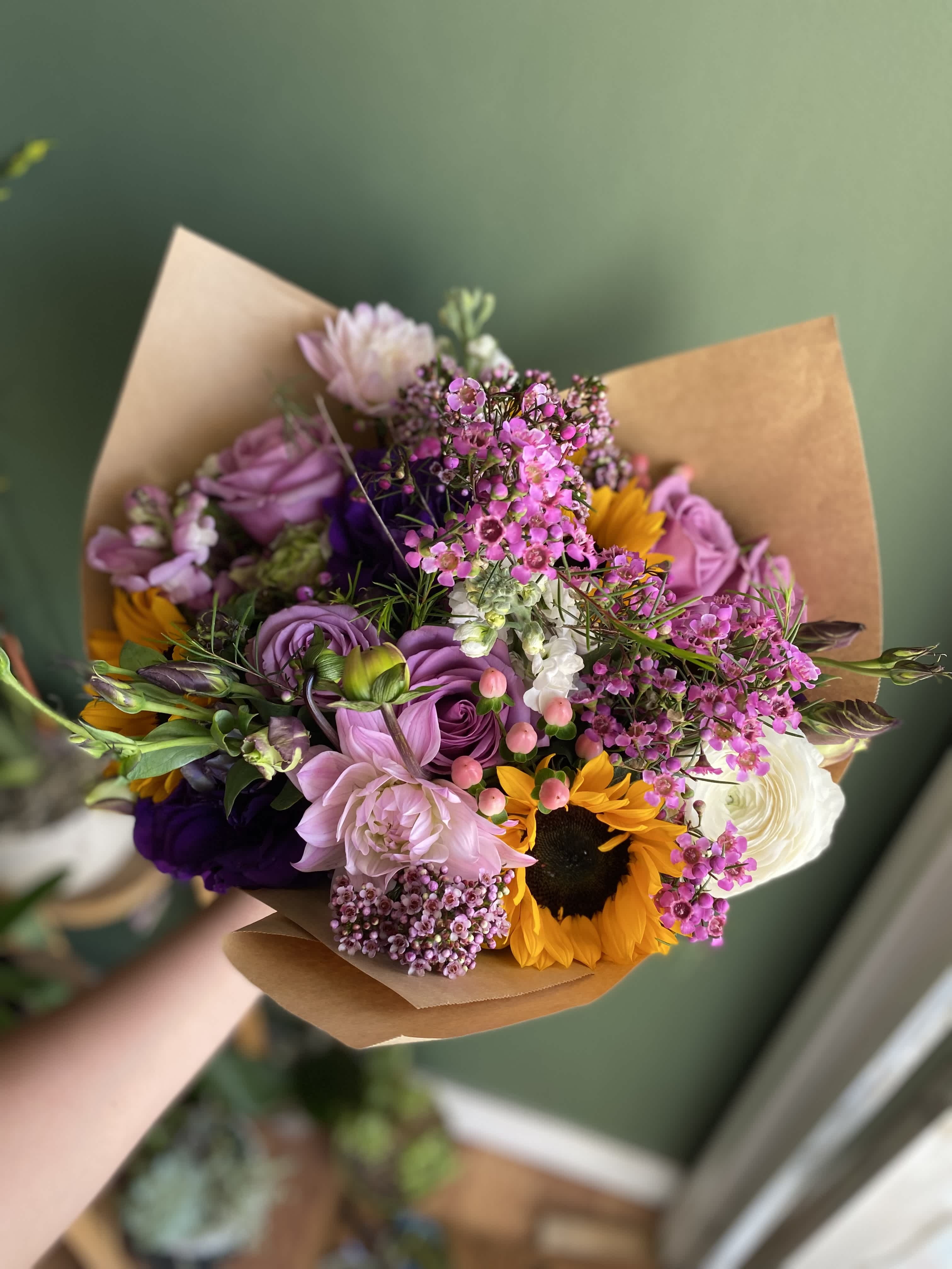 Handheld bouquet of pink, purple, white, and yellow flowers wrapped in brown paper