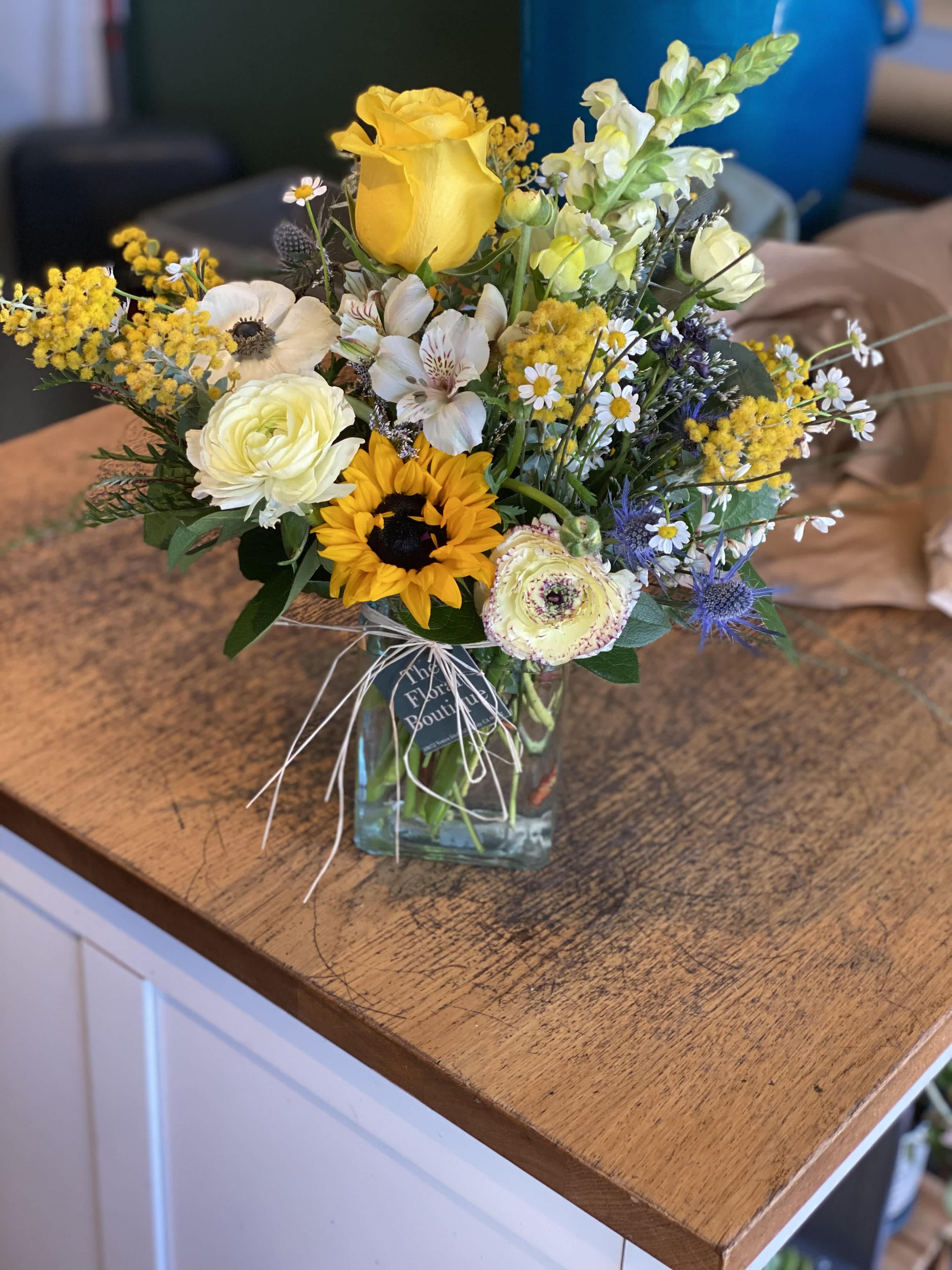 Mixed bouquet with yellow roses, sunflower, and white blooms in a glass vase