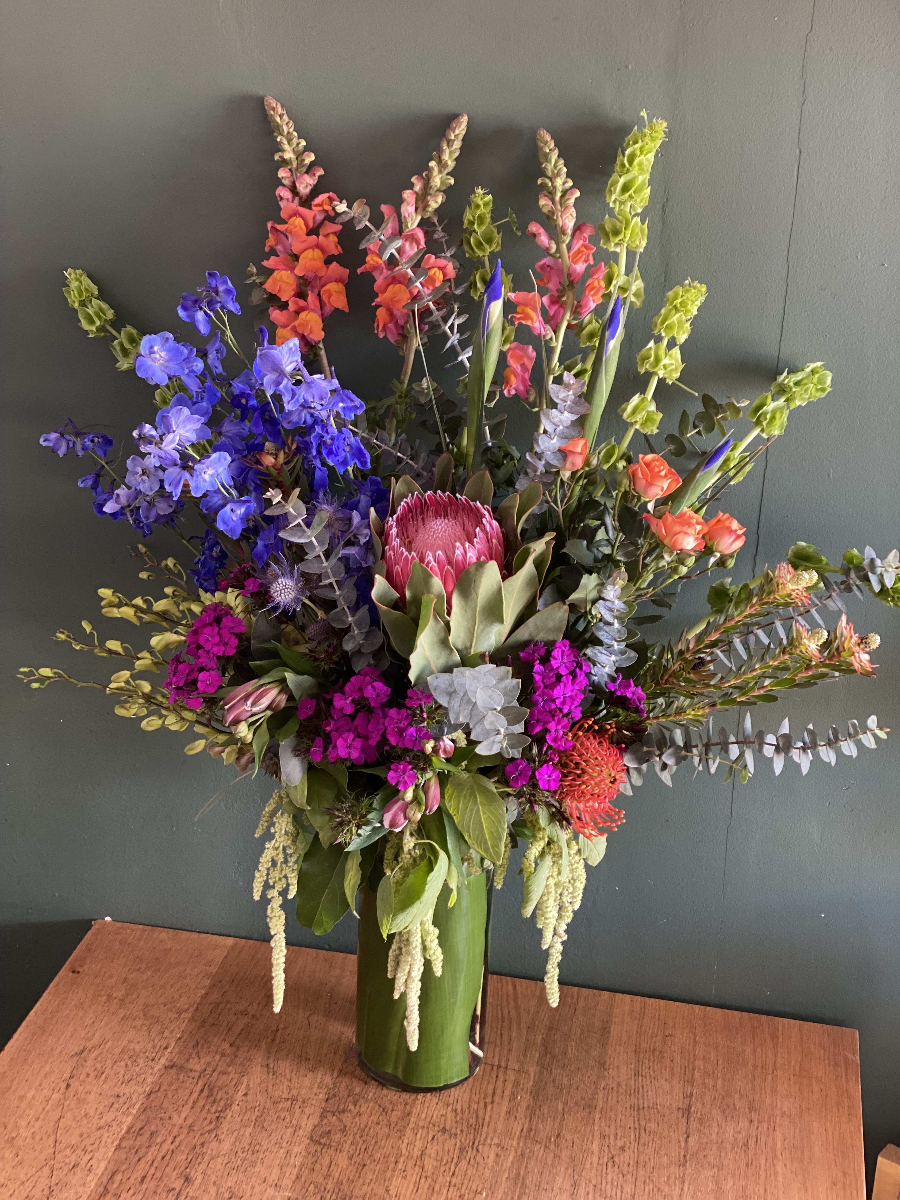 Tall mixed flower arrangement in a green vase with bright pink, blue, and orange blooms