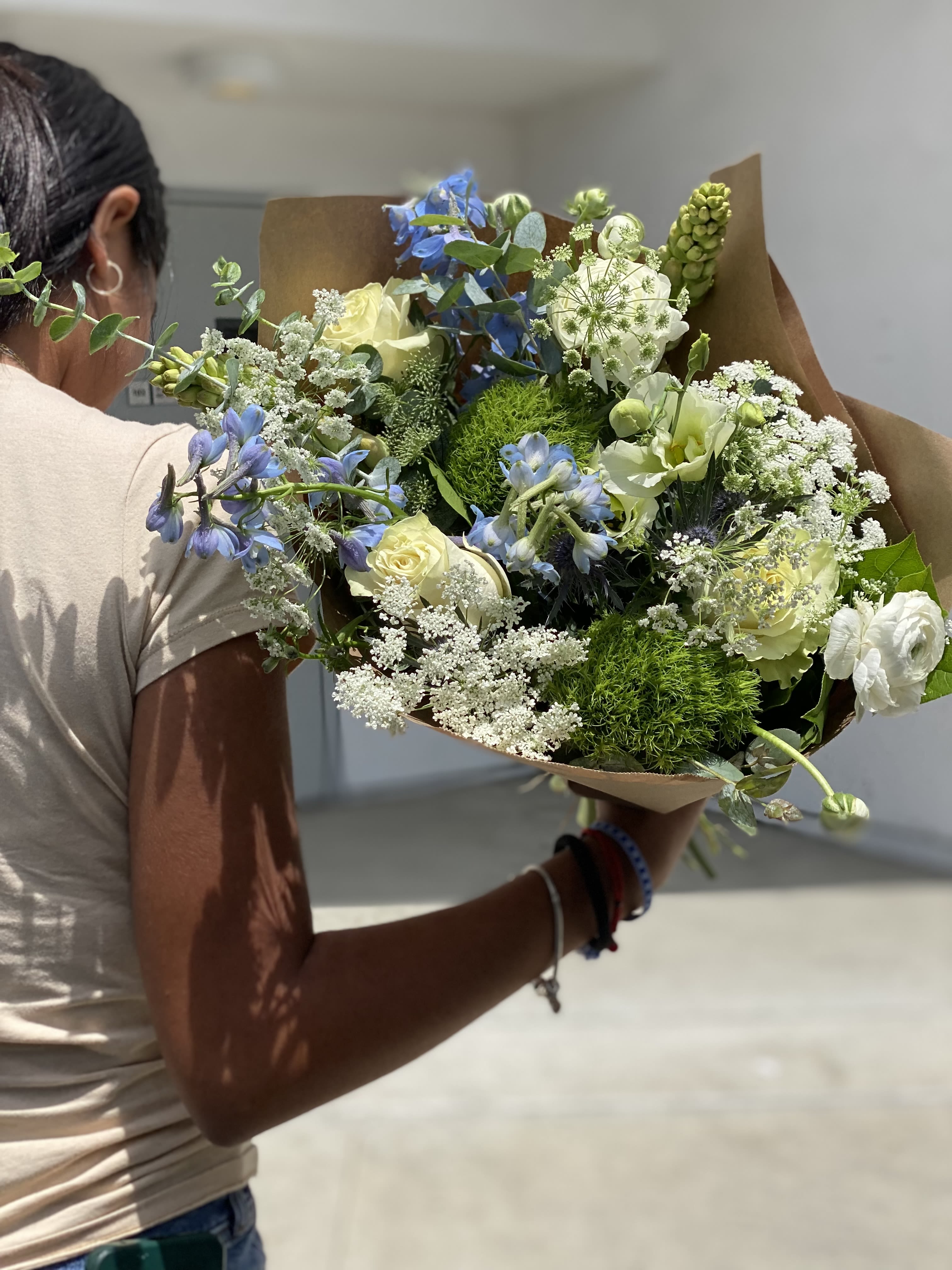 Handheld bouquet of blue, white, and pale yellow flowers wrapped in brown paper