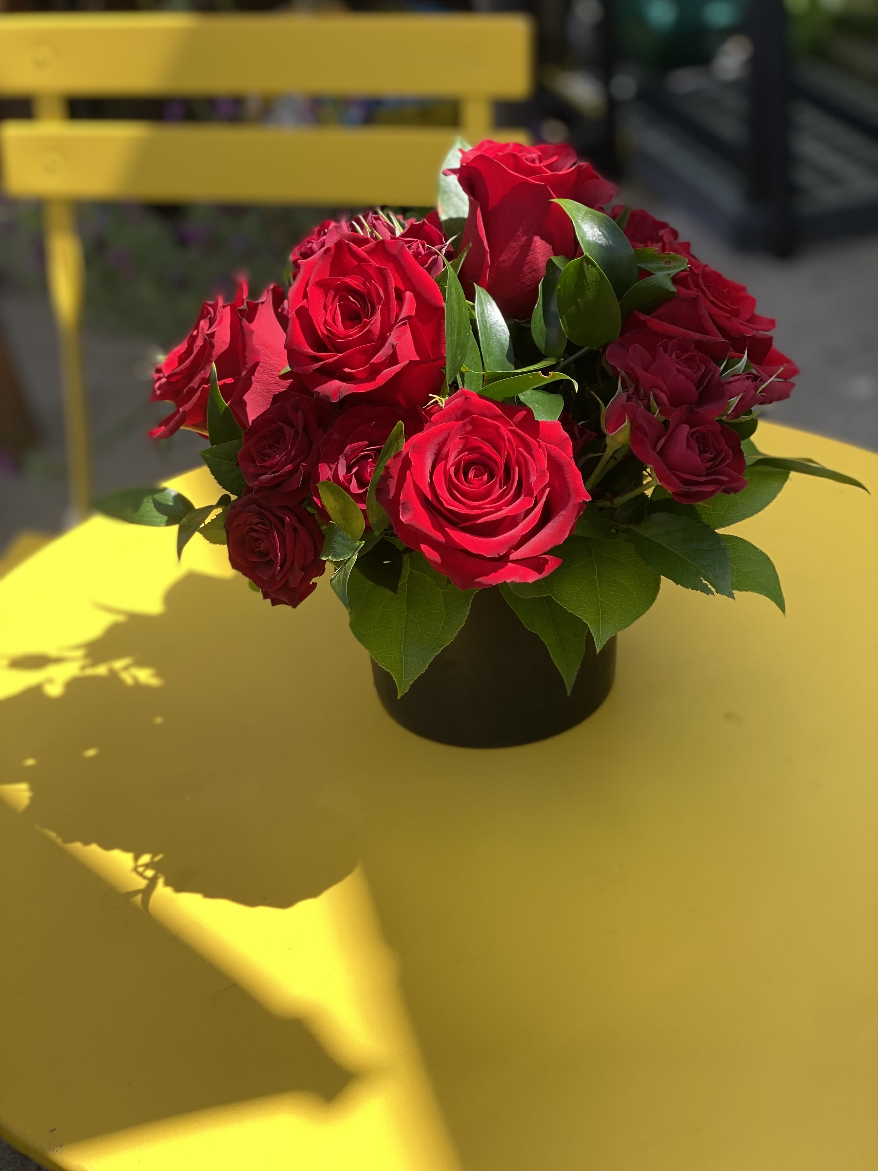 Red roses arranged in a black vase on a yellow table
