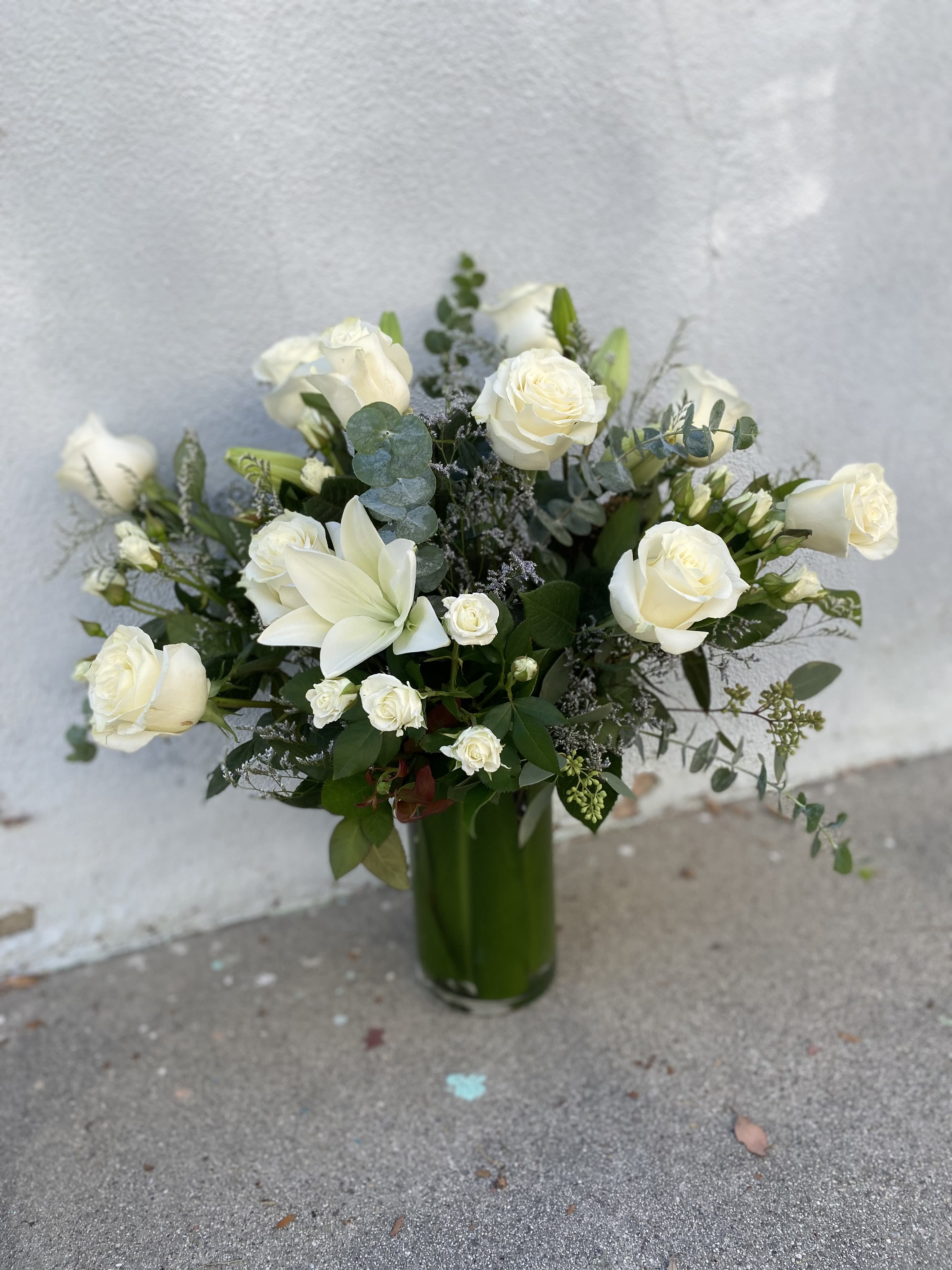 White roses and lilies arranged in a tall green vase
