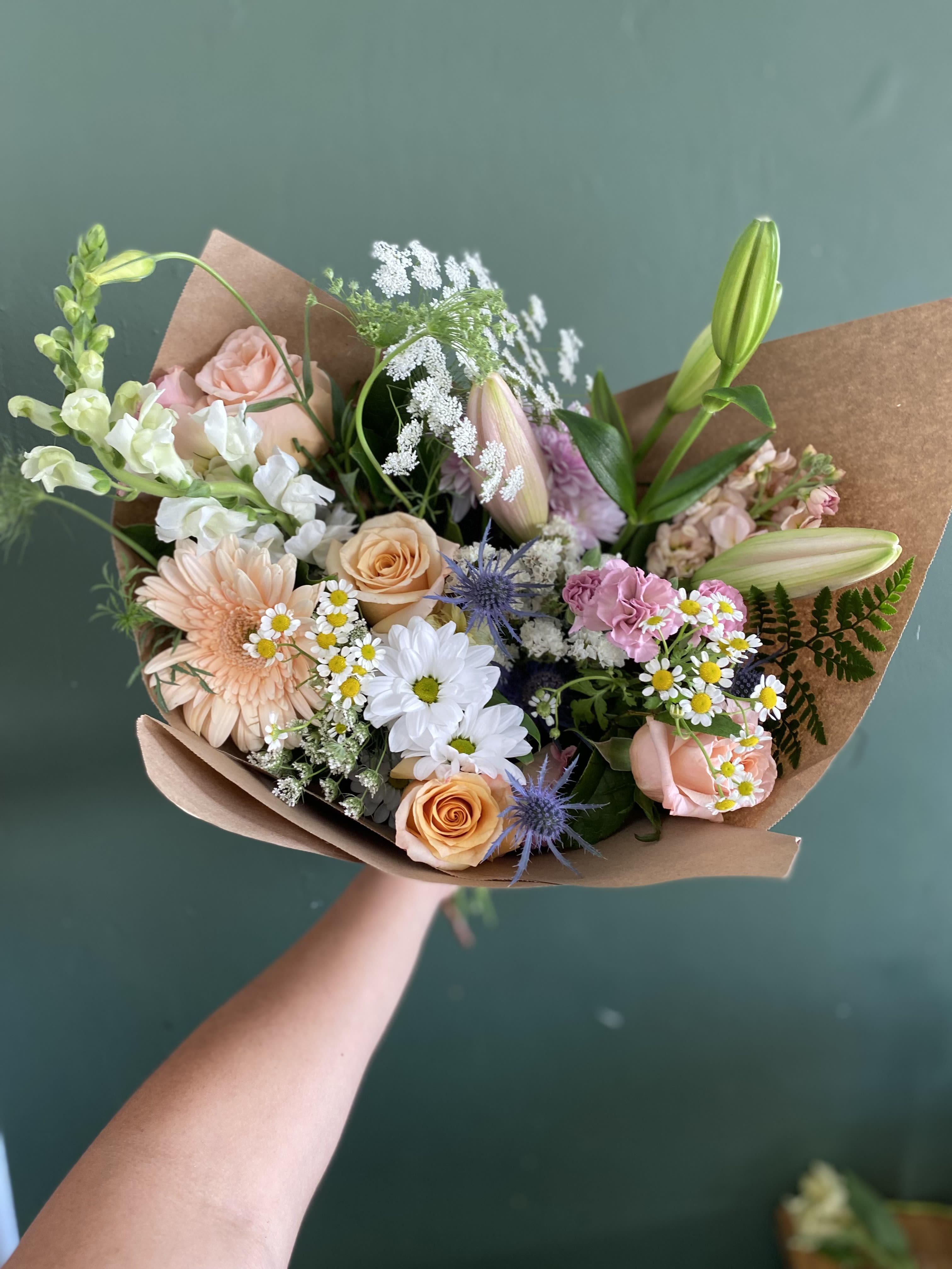 Handheld bouquet of pastel flowers wrapped in brown paper