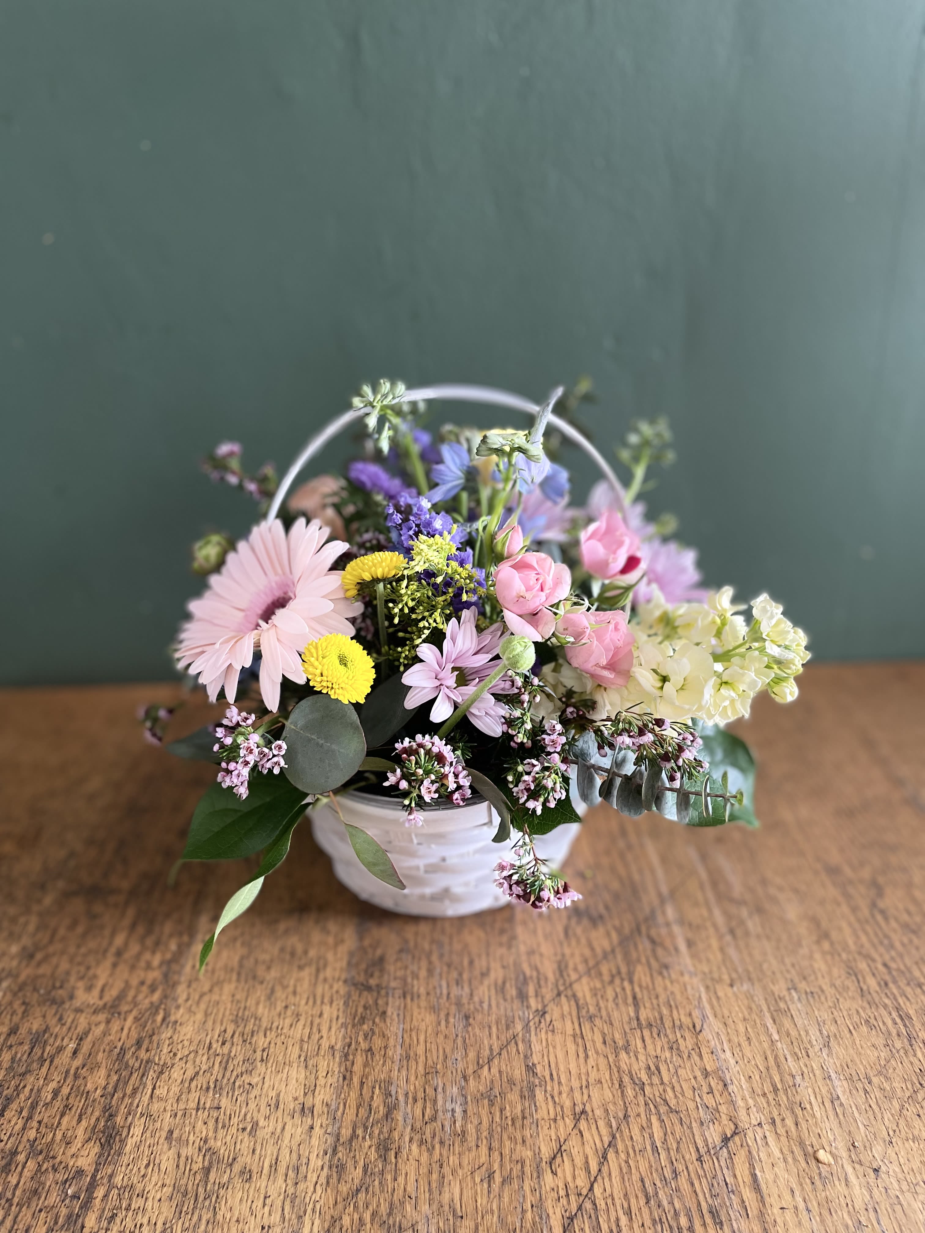 Pastel mixed flower arrangement in a white basket with a handle