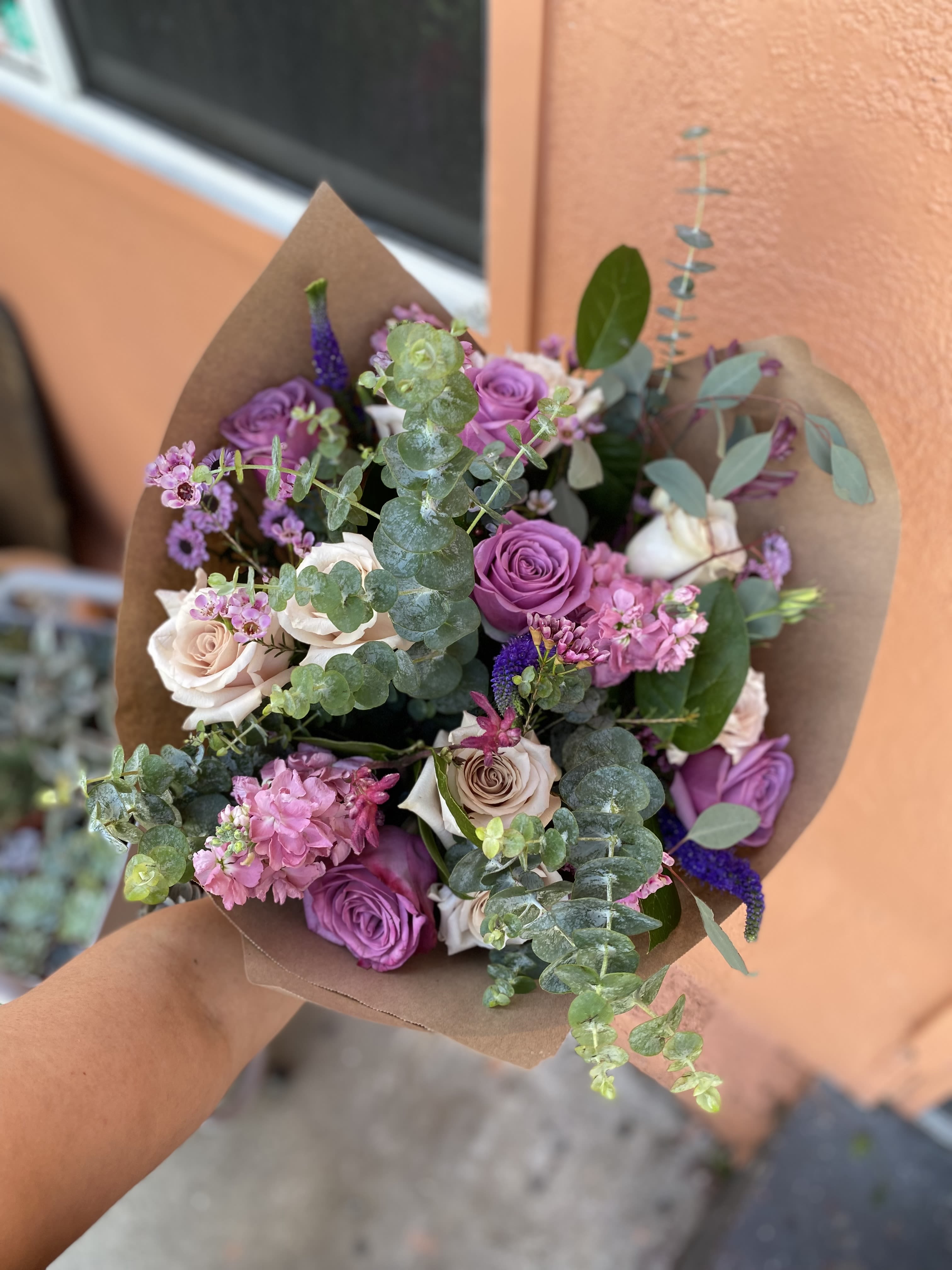 Handheld bouquet of purple and blush roses with eucalyptus in brown paper