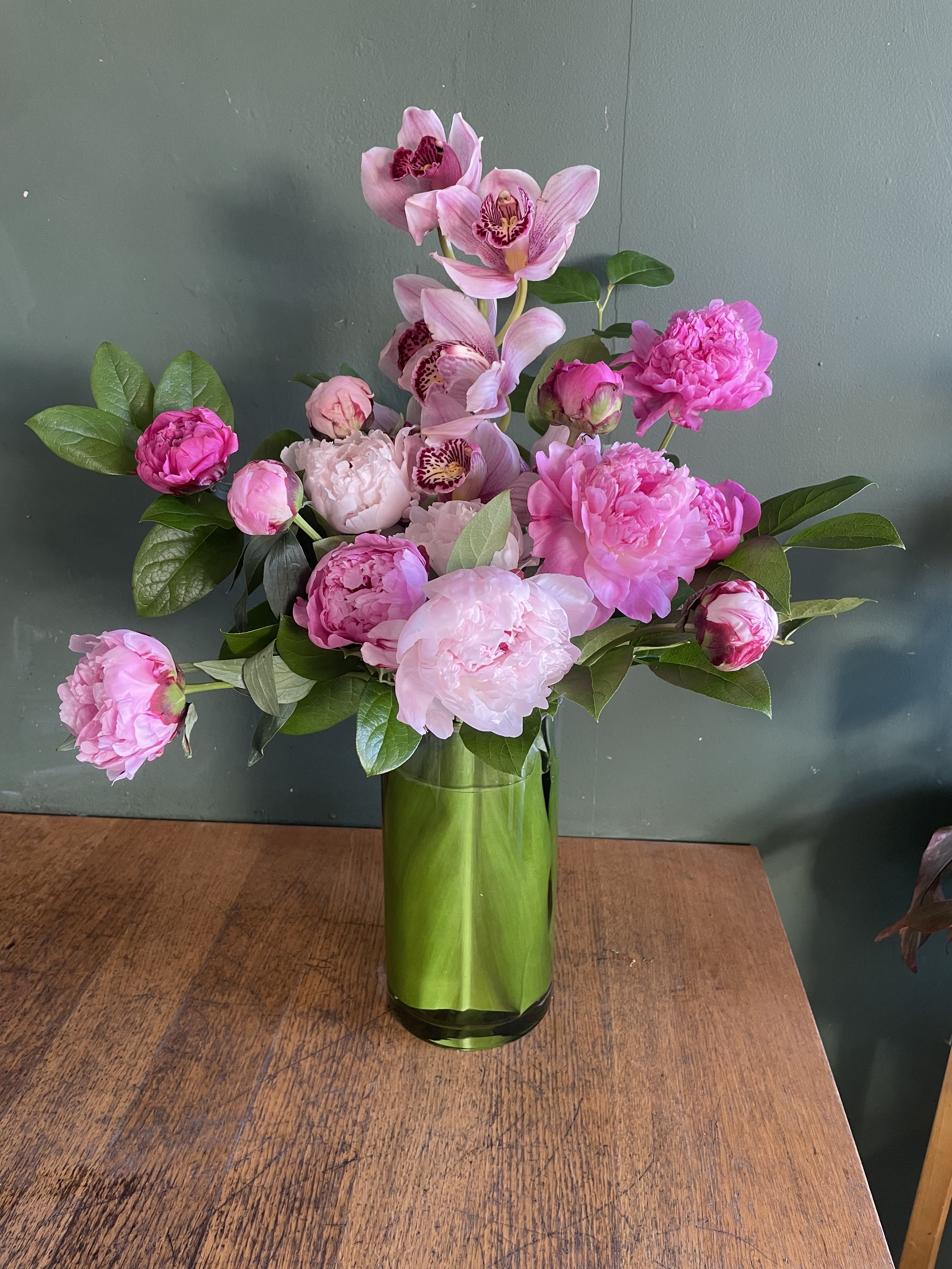 Pink peonies and orchids arranged in a green glass vase