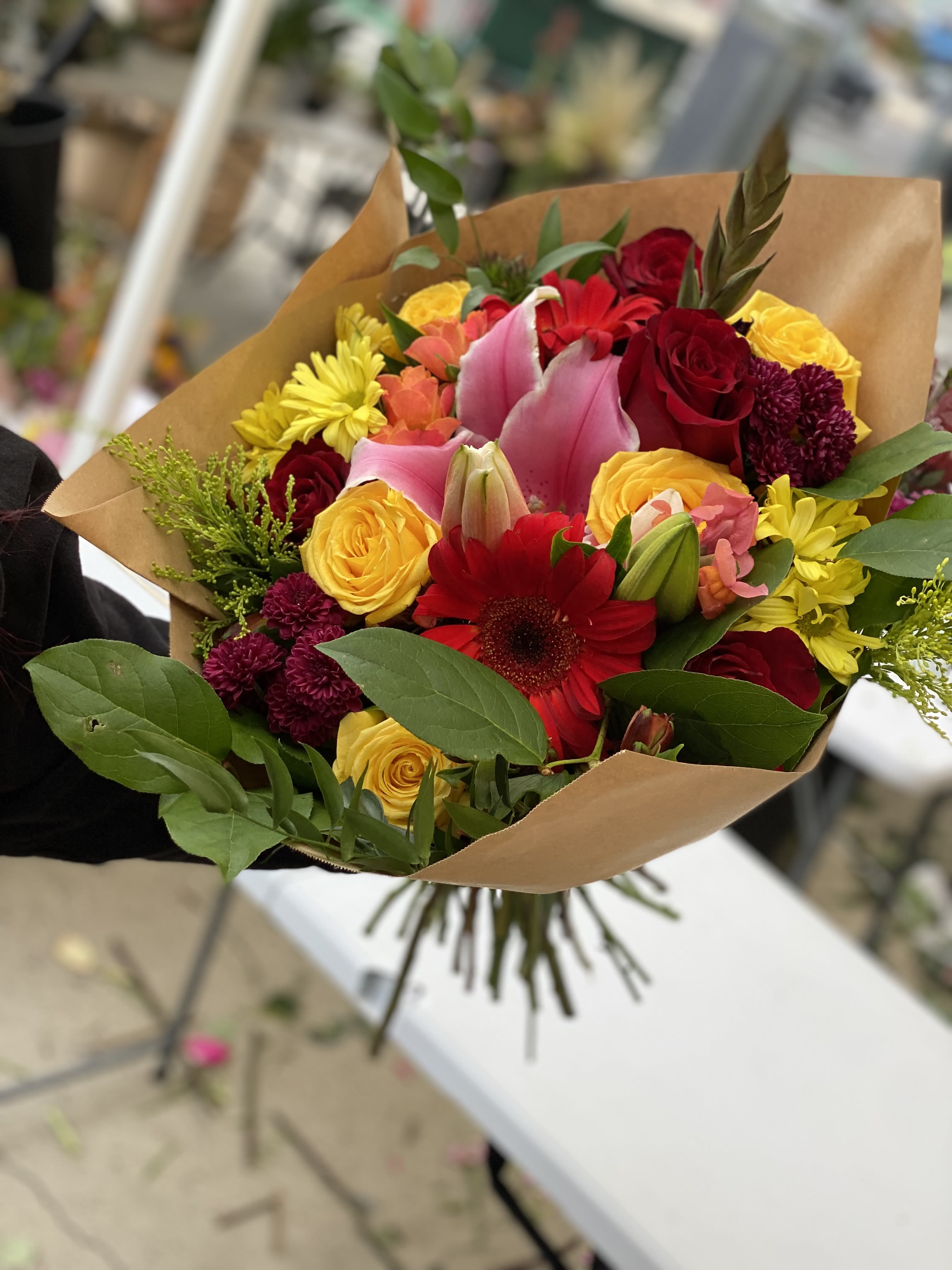 Mixed bouquet of roses, lilies, and daisies wrapped in brown paper