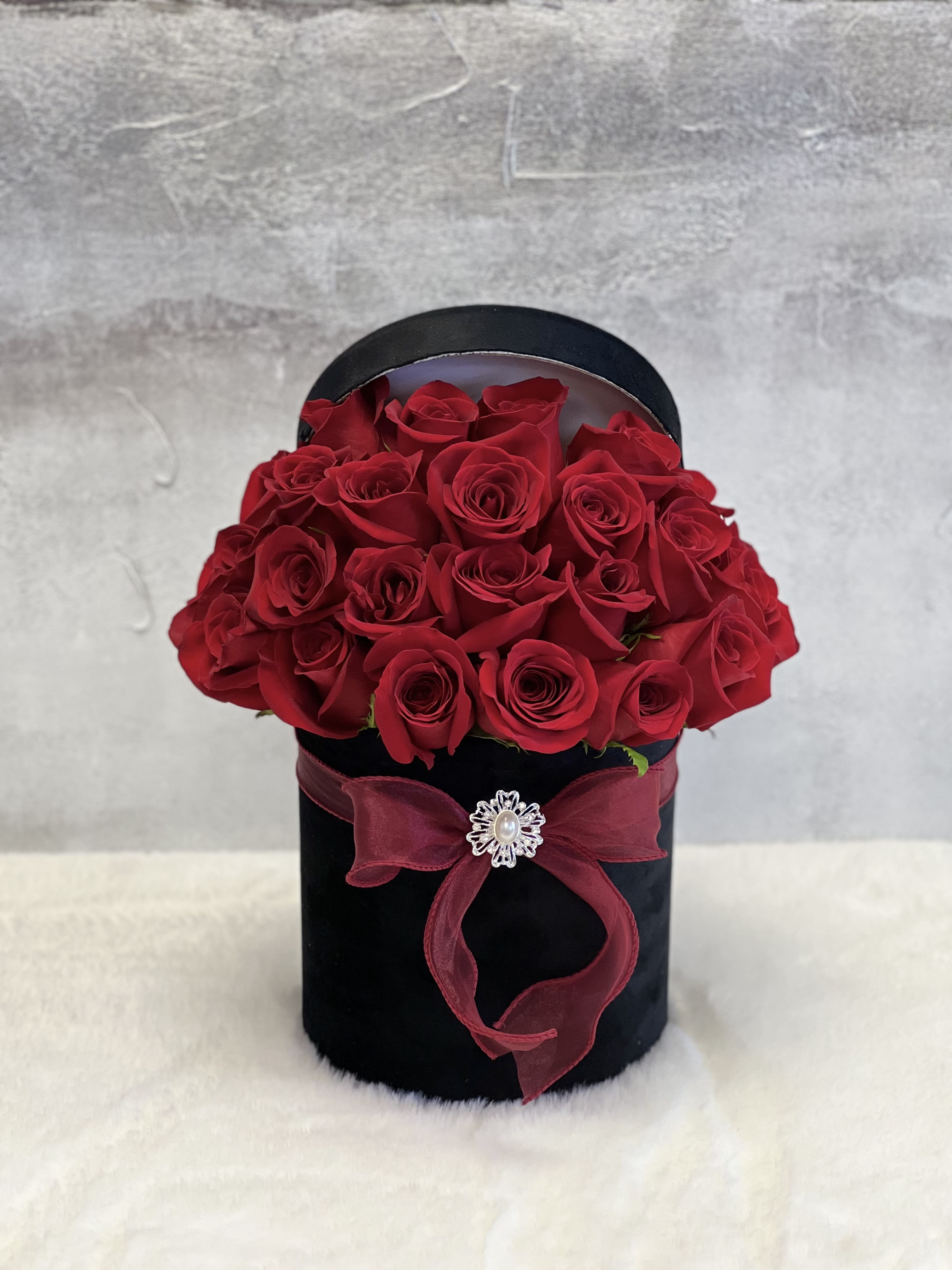 Round black hatbox filled with red roses, tied with a red bow and jeweled brooch.
