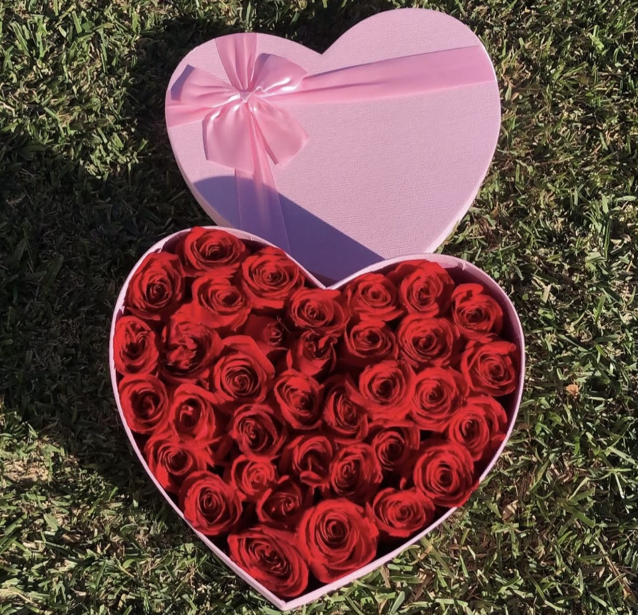 Heart-shaped pink box filled with red roses and a pink ribbon bow
