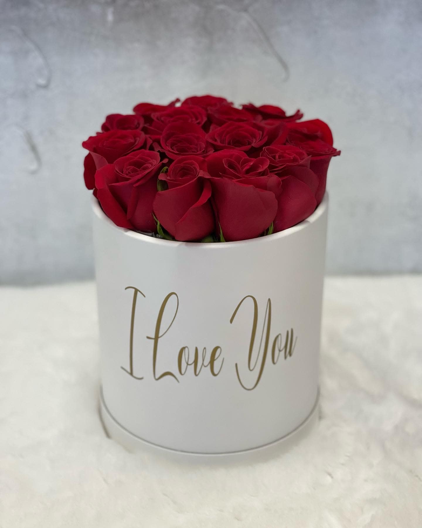 Round white hatbox filled with red roses and gold script reading I Love You.