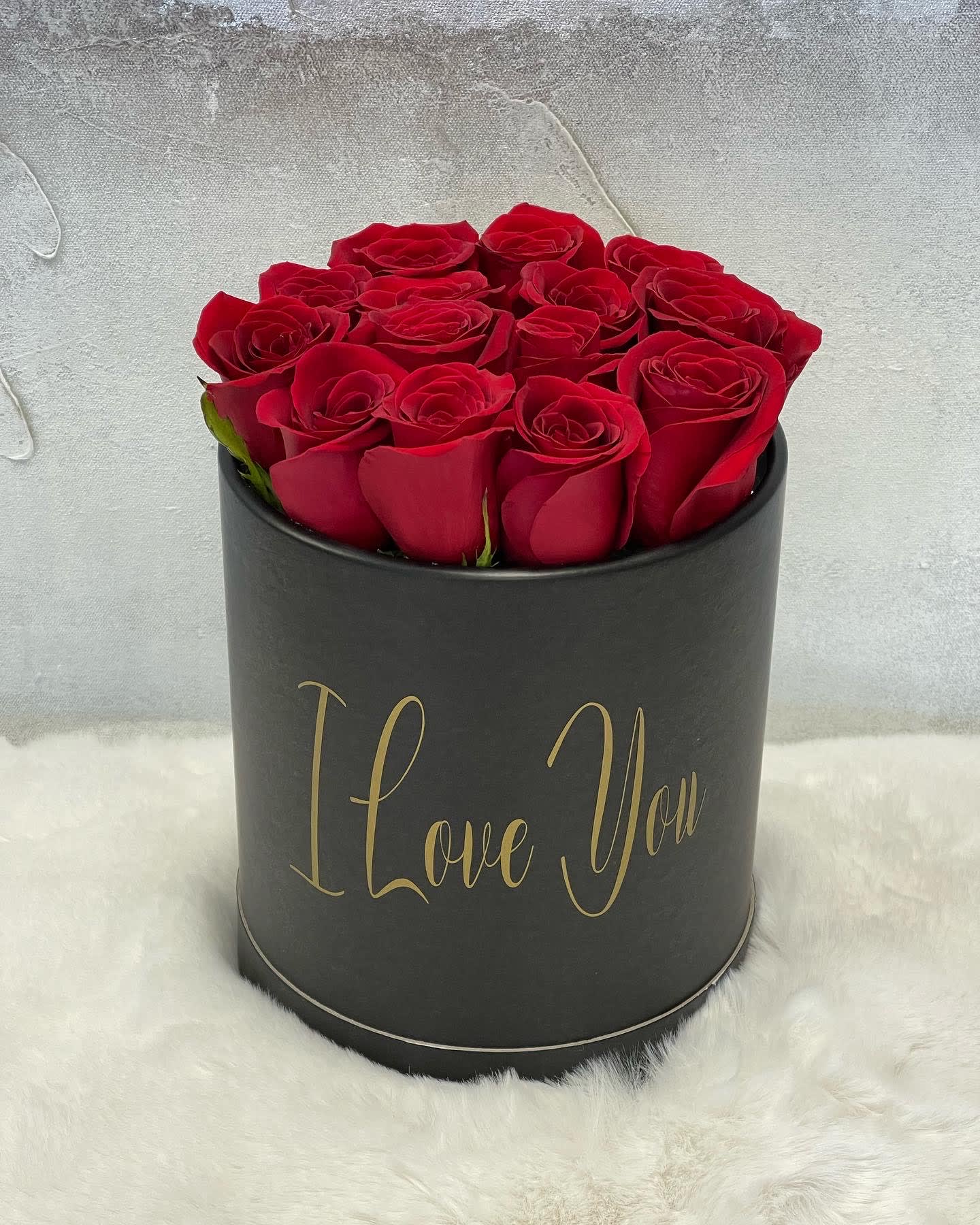 Black hatbox of red roses with gold 'I Love You' text, displayed on white fur.