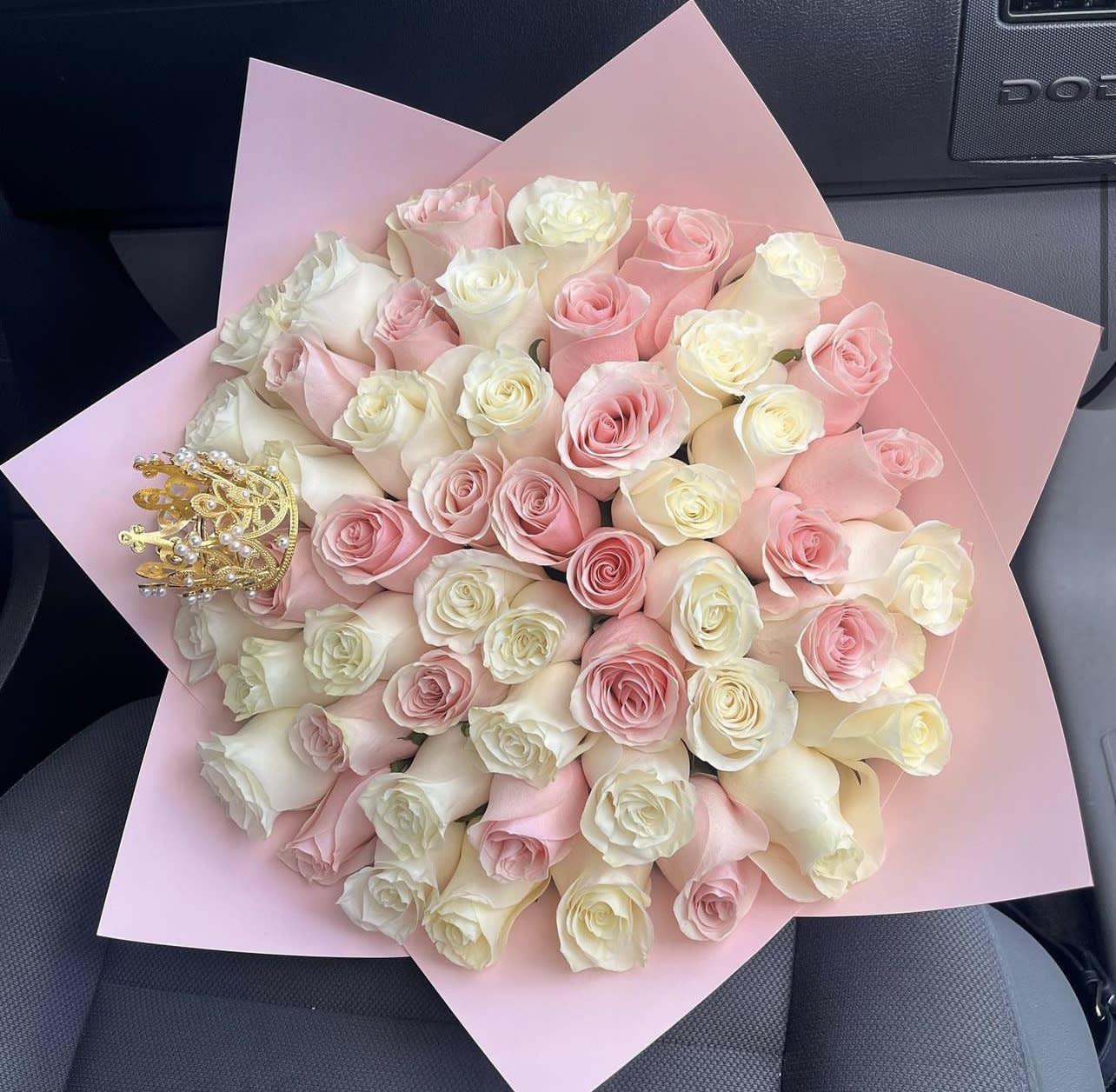 Bouquet of pink and ivory roses wrapped in pink paper with a small decorative crown accent