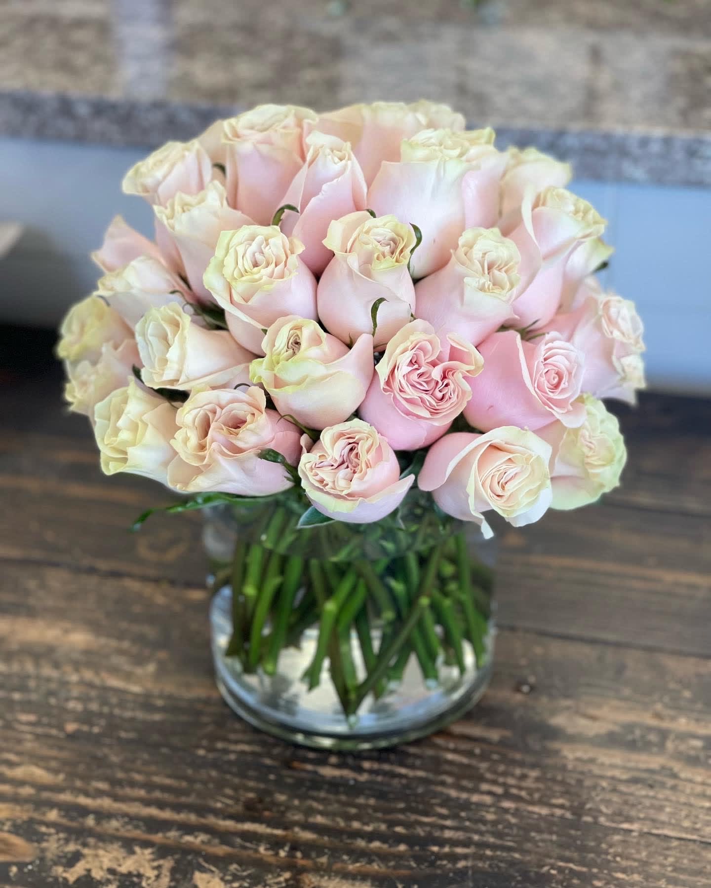 Compact arrangement of pale pink roses clustered in a clear glass cylinder vase