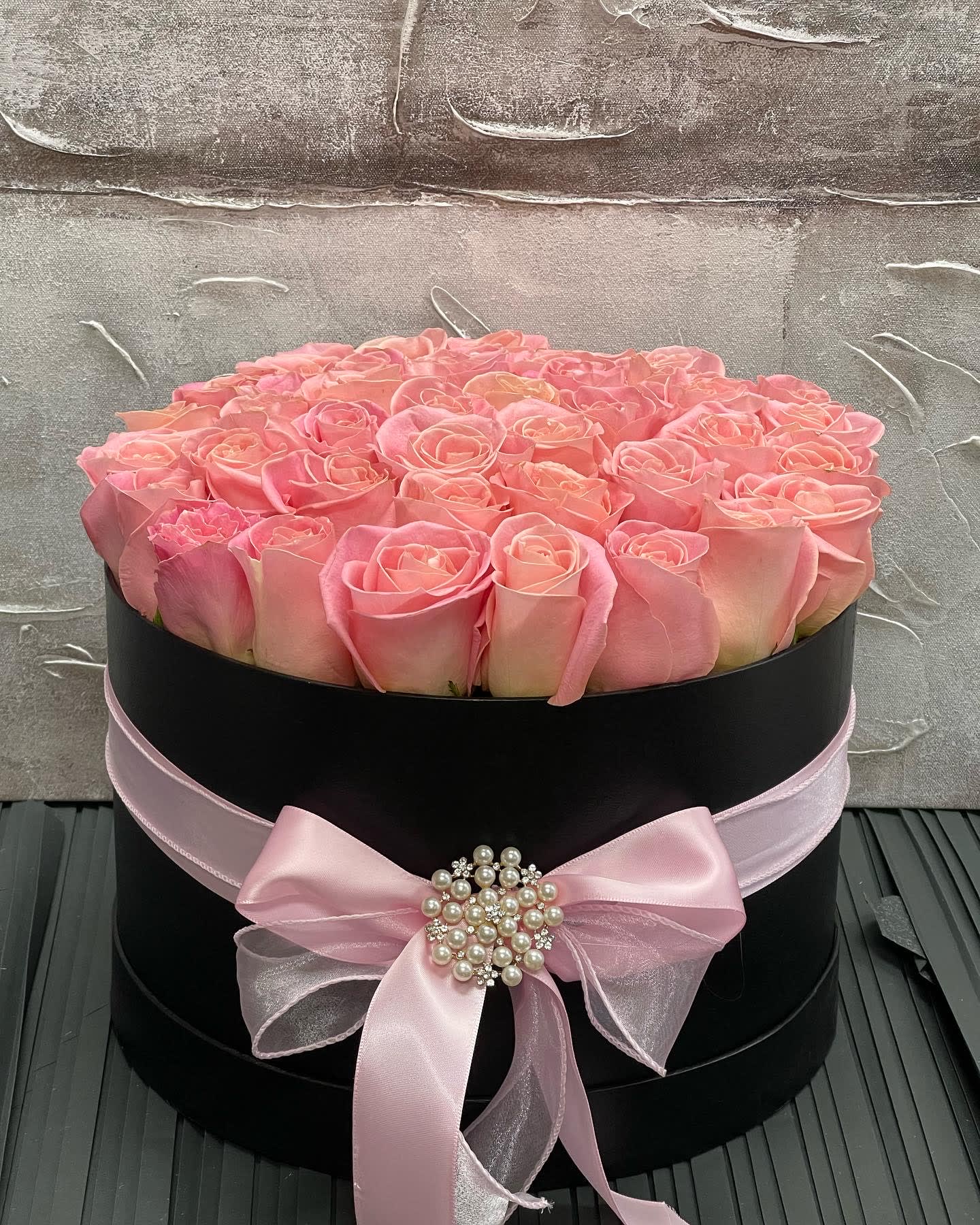 Round black hatbox filled with pink roses and tied with a pink ribbon bow