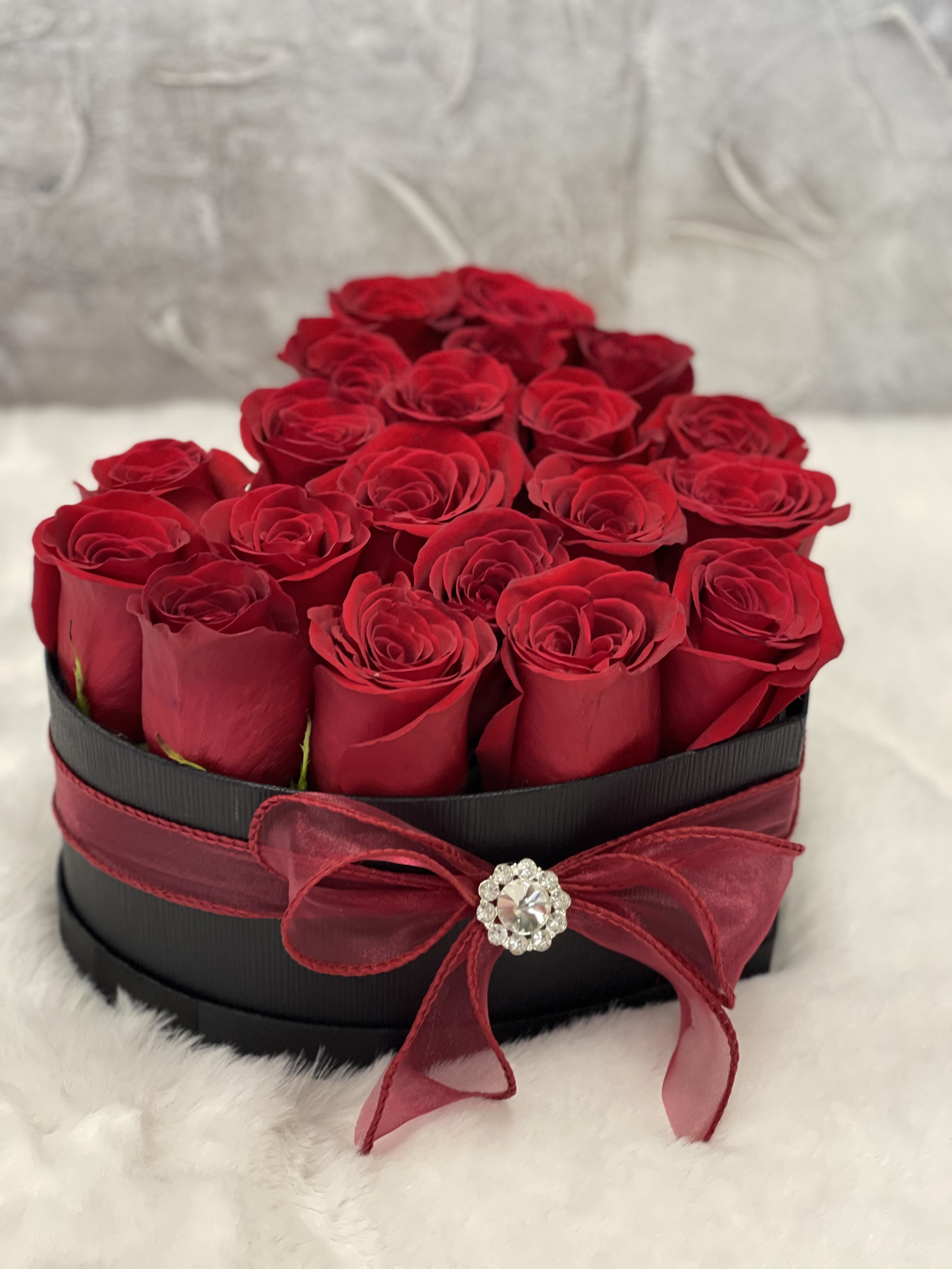 Heart-shaped black box filled with red roses and tied with a red bow and jewel accent