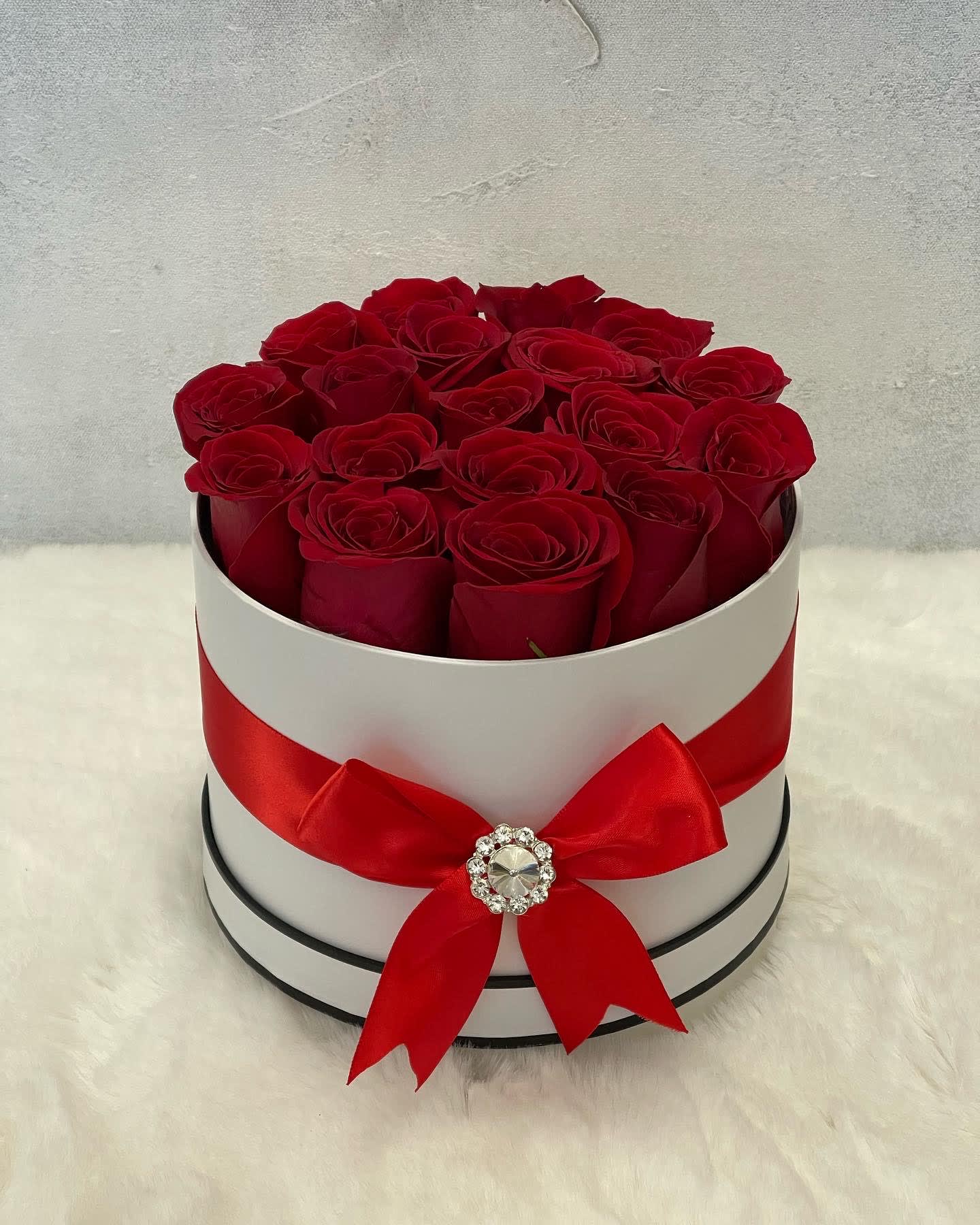 Round white hatbox of red roses with a red ribbon bow on a soft white surface