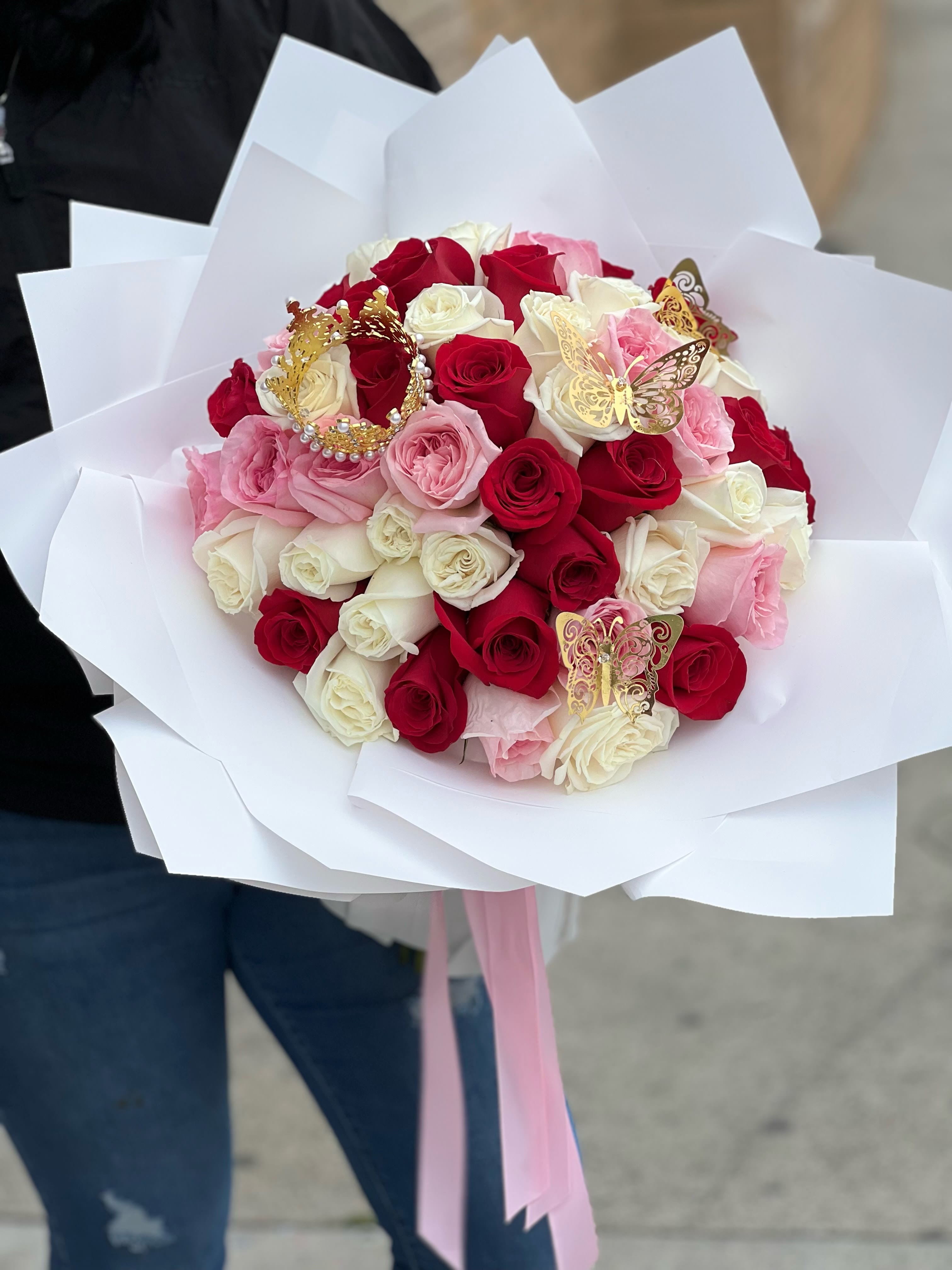 Large bouquet of red, white, and pink roses wrapped in white paper with gold butterflies and a crown