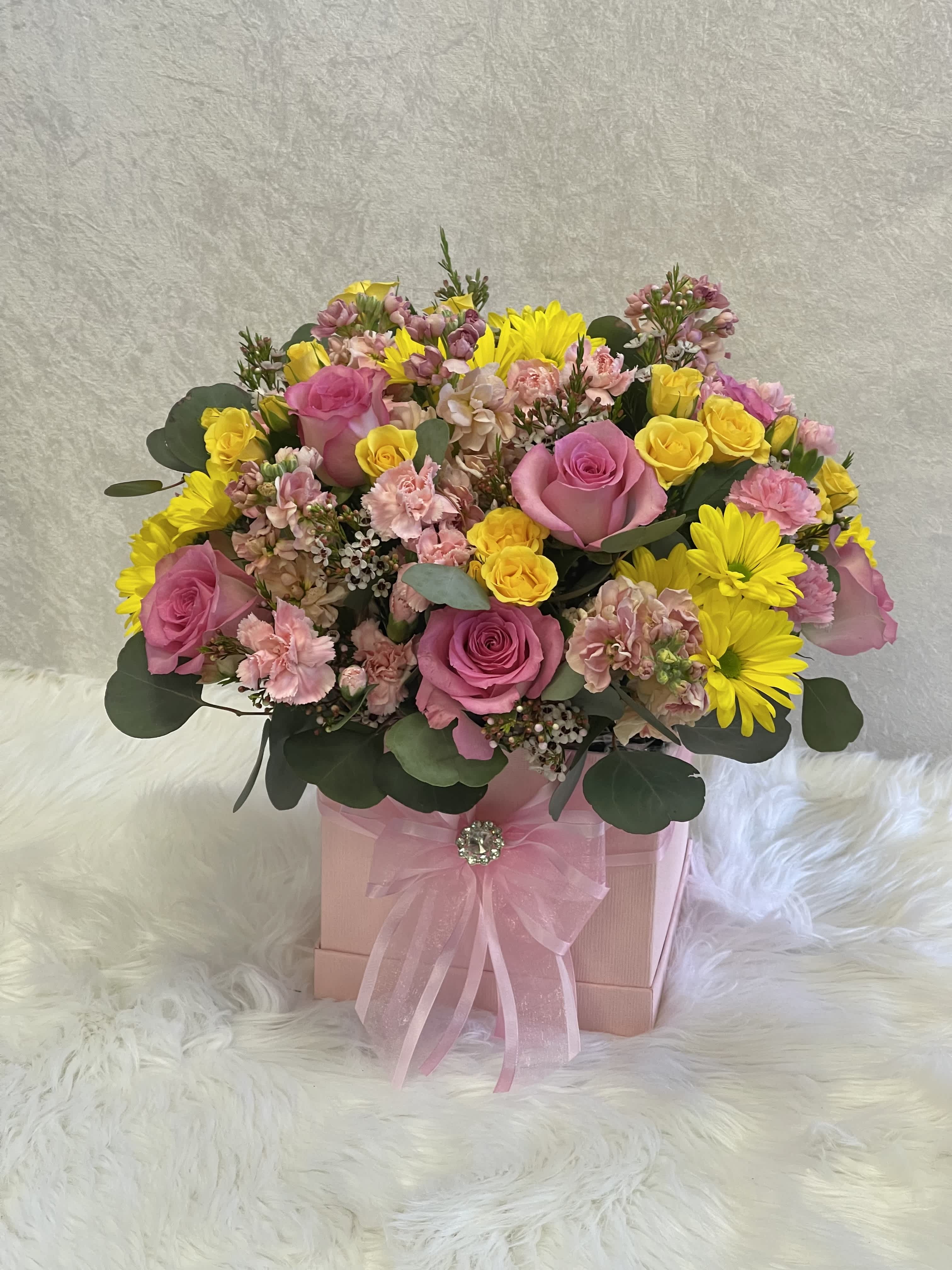 Pink and yellow mixed flower arrangement in a pink gift box with ribbon