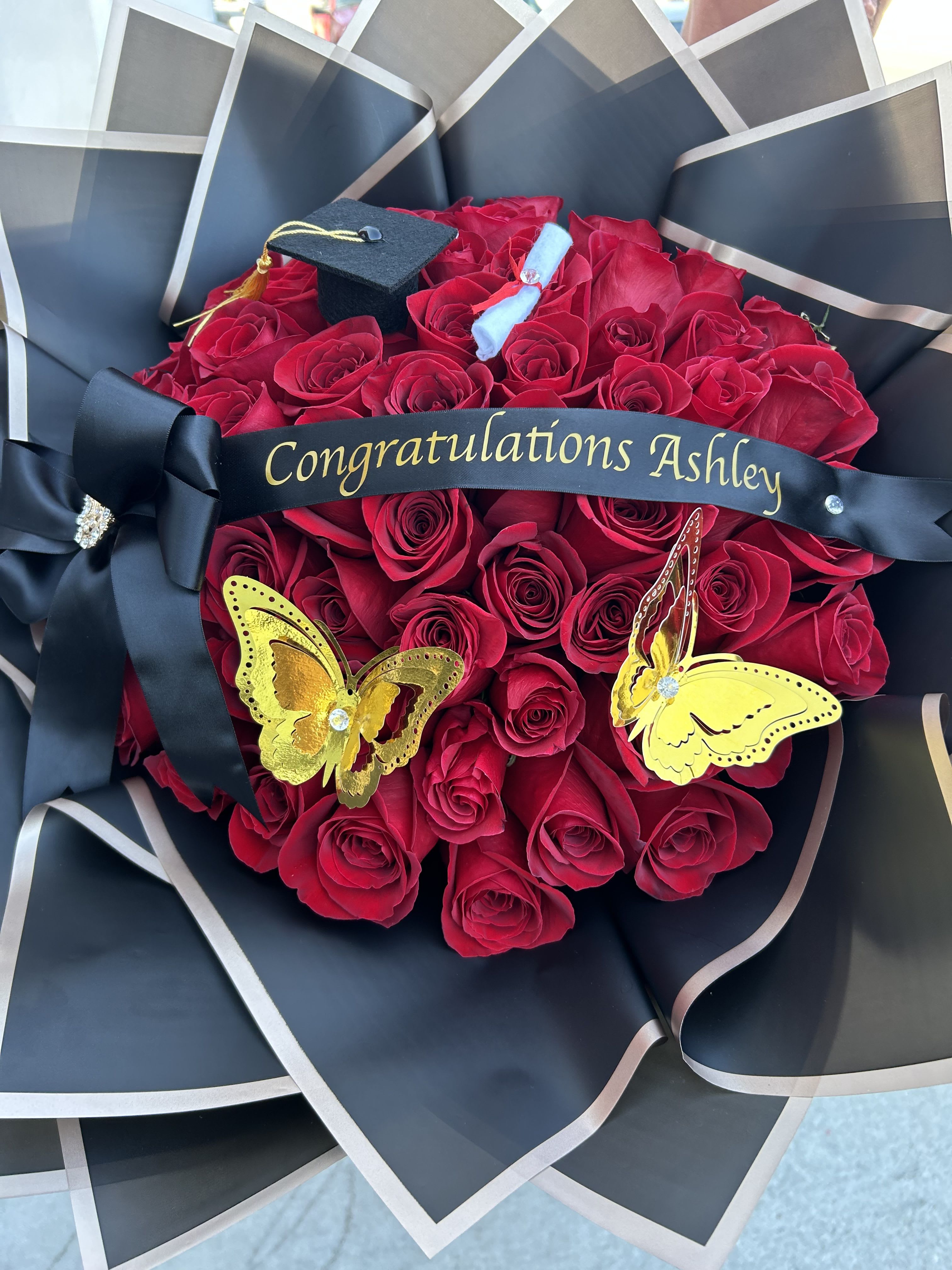 Red rose bouquet with a graduation cap and black ribbon reading Congratulations Ashley