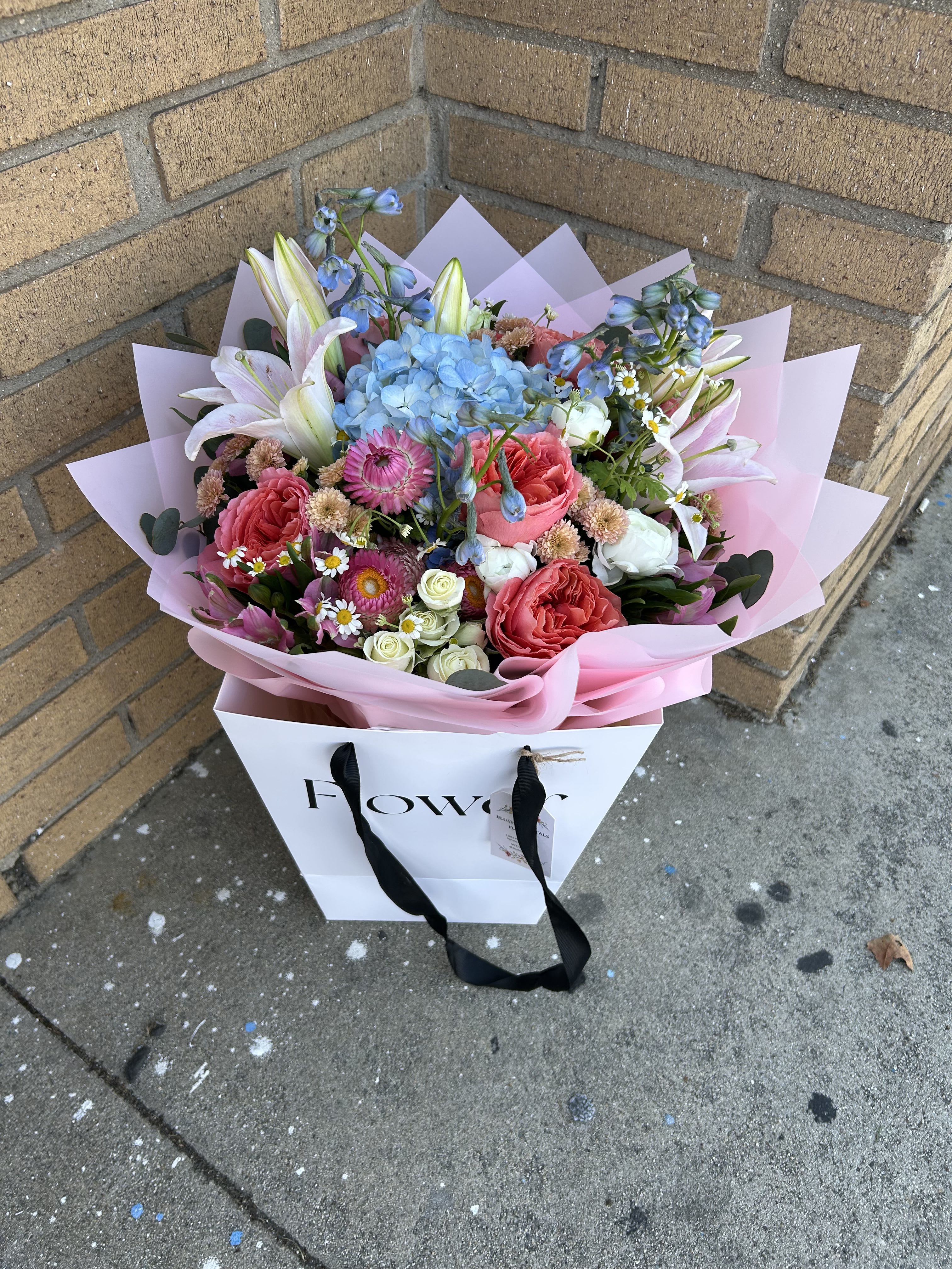 Mixed bouquet with pink roses, blue hydrangea, and white lilies in pink wrap
