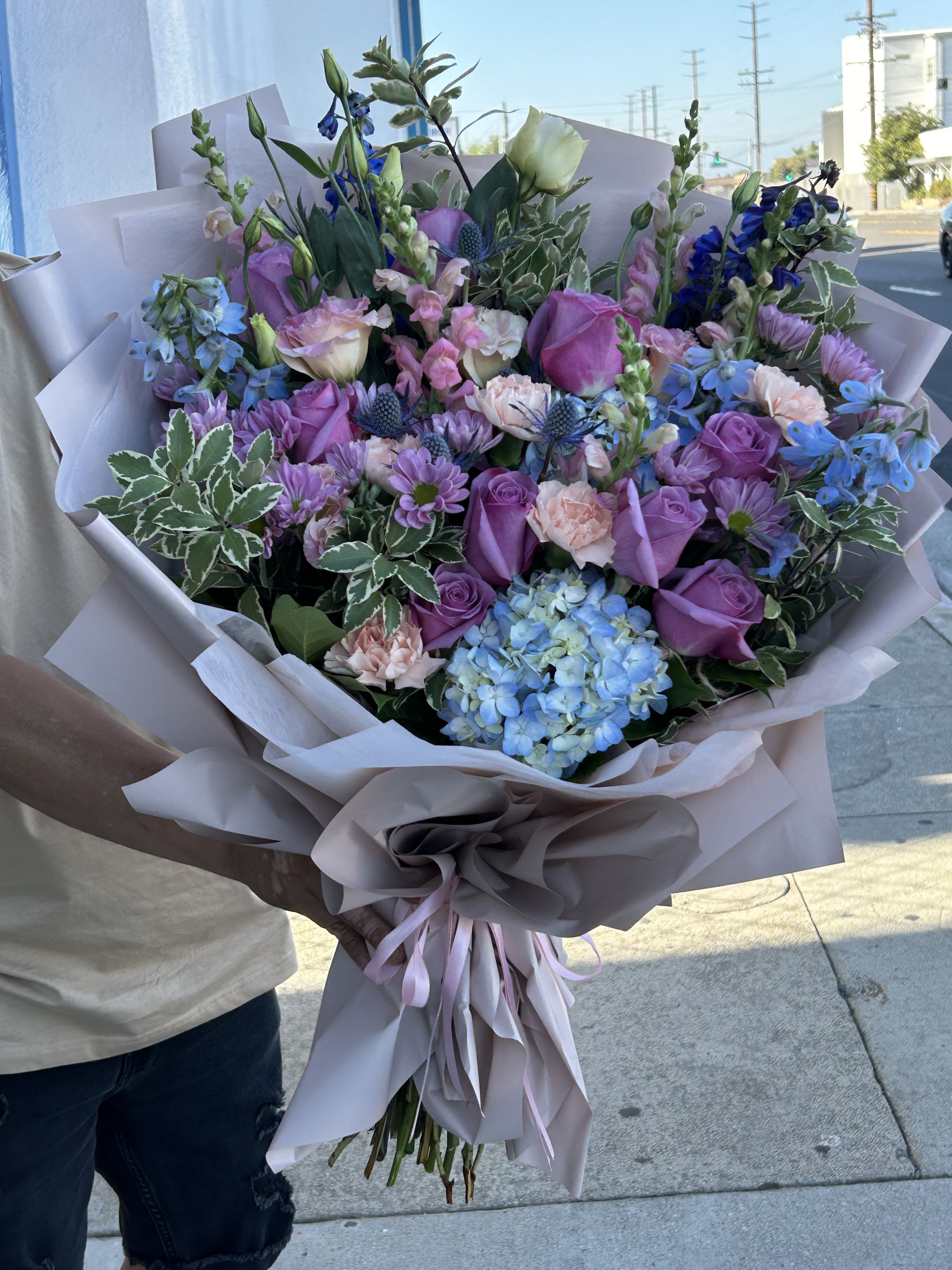 Large bouquet of purple, pink, and blue flowers wrapped in pale paper
