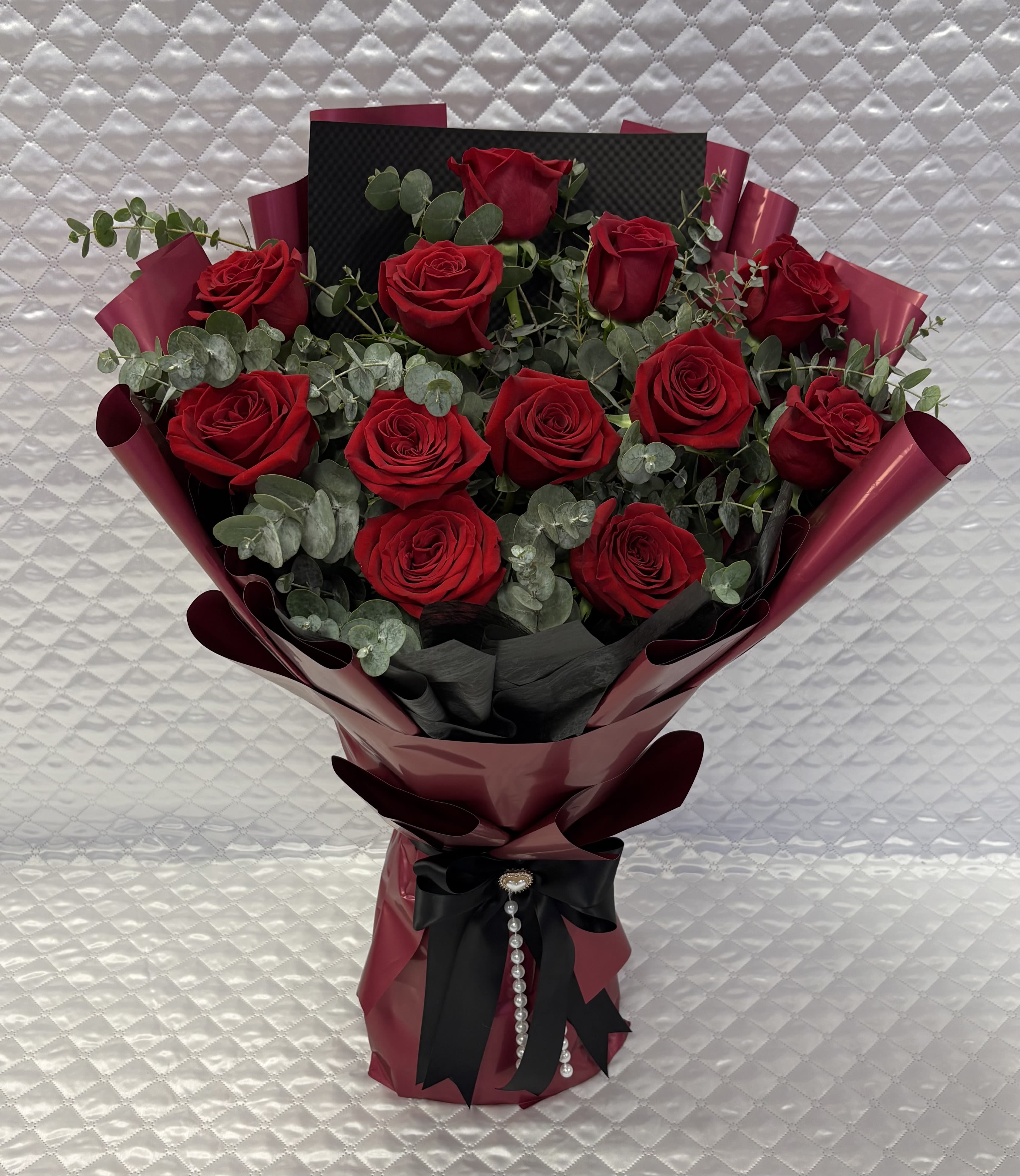Bouquet of red roses wrapped in burgundy paper with a black ribbon