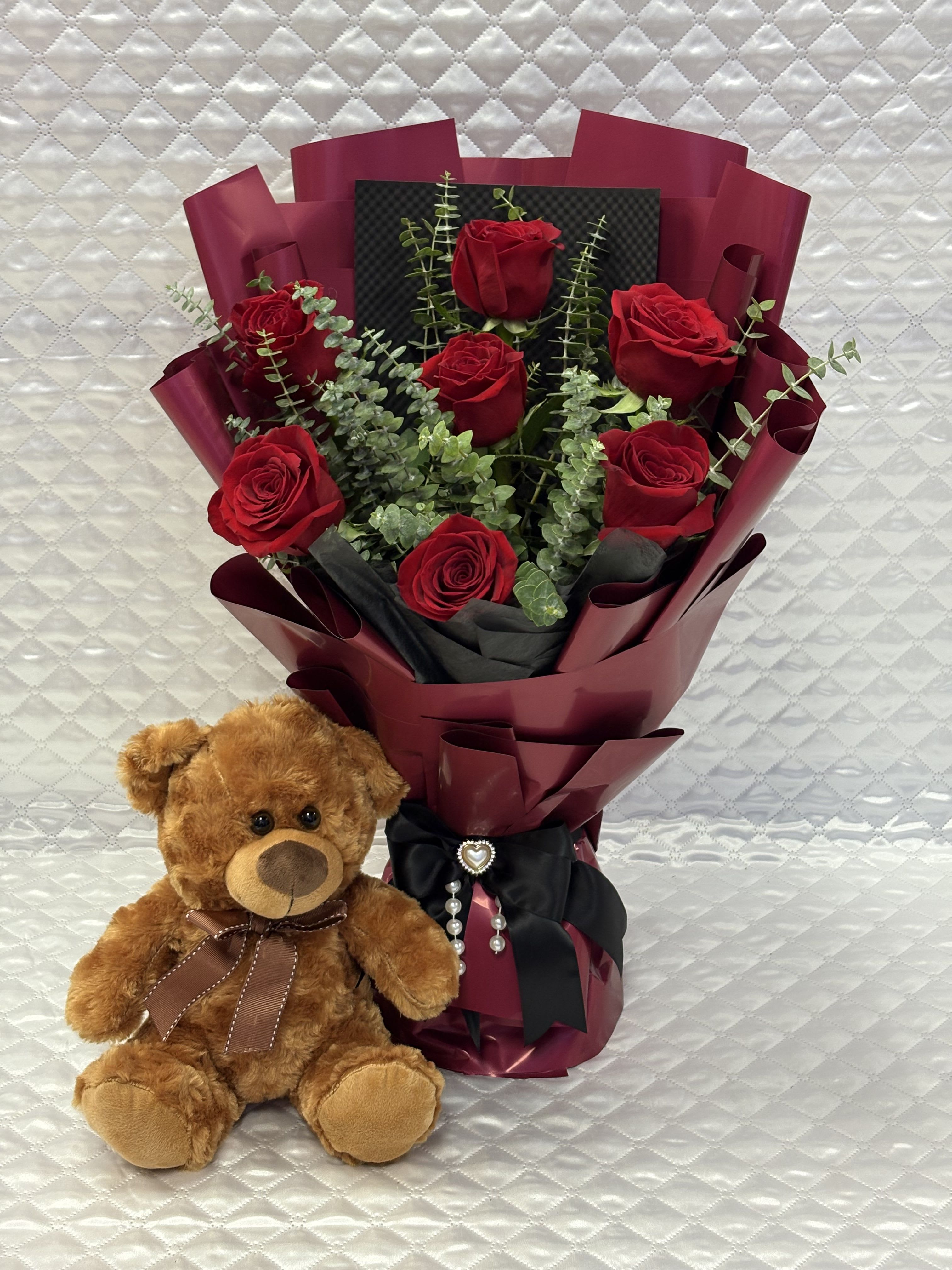 Bouquet of red roses with a teddy bear beside it
