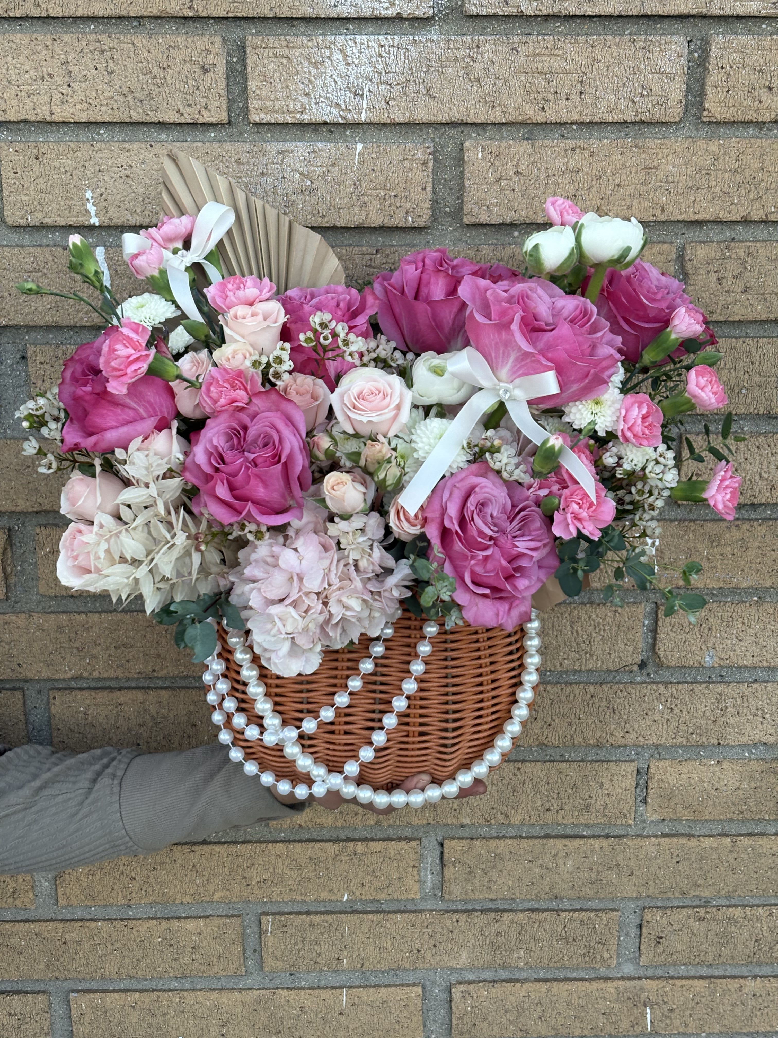 Pink rose bouquet in a wicker basket with white ribbon and pearl strands