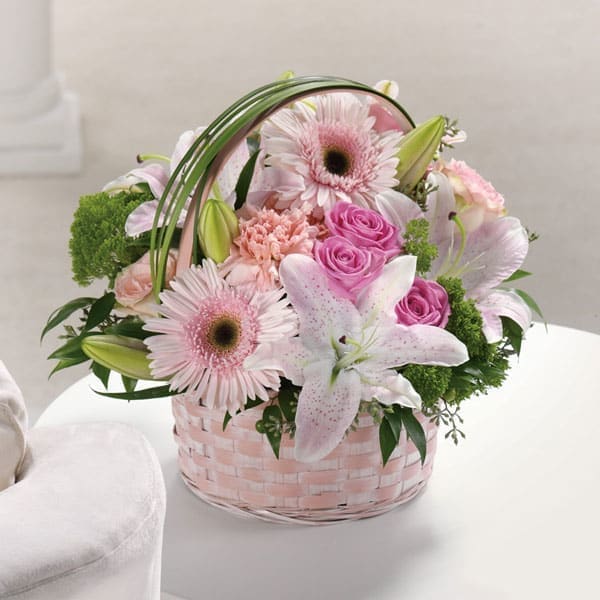 Pink and white lilies, roses, and gerbera daisies arranged in a pastel basket.