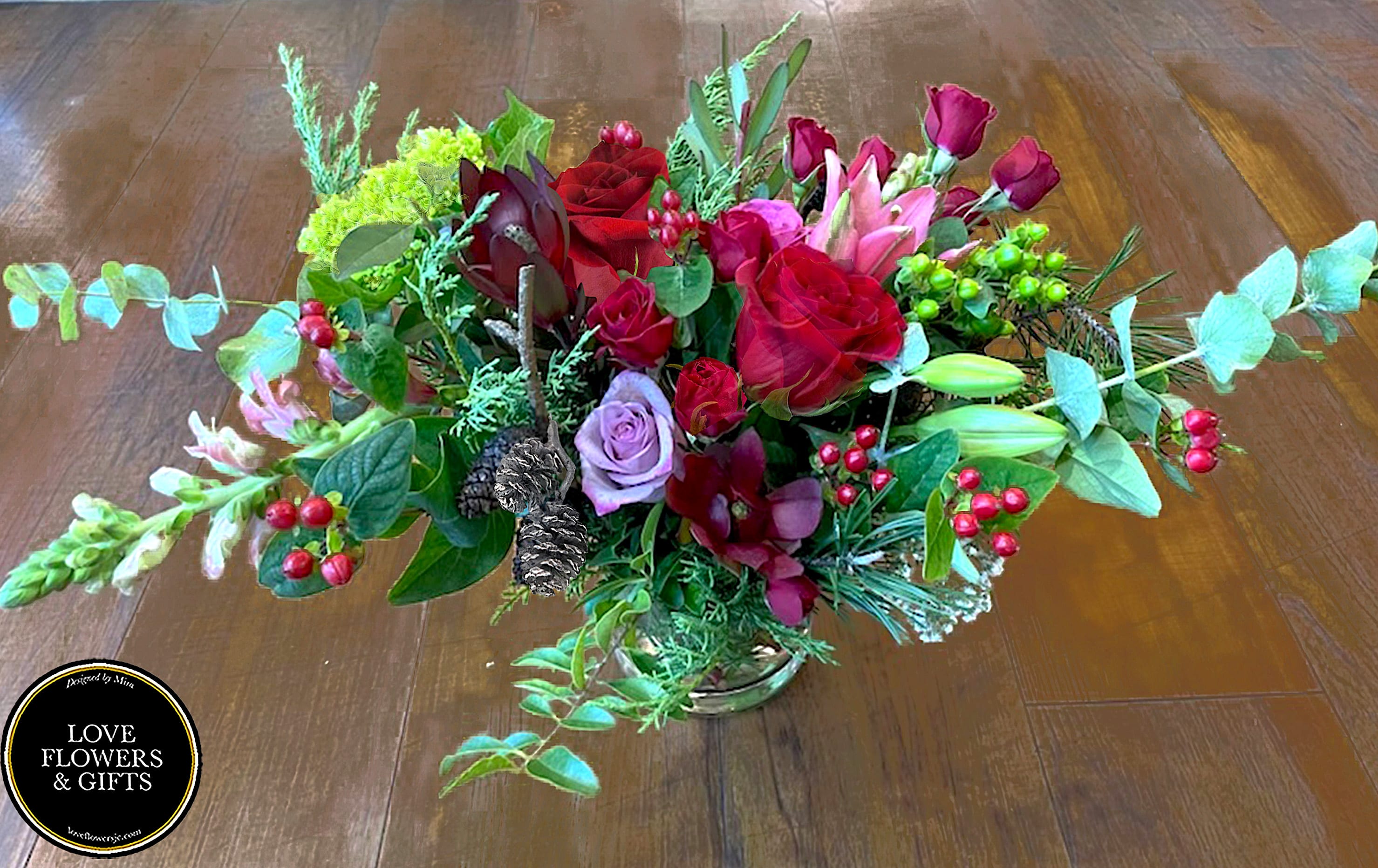 Low centerpiece of red roses, pink lilies, berries, and pine cones in a clear glass vase