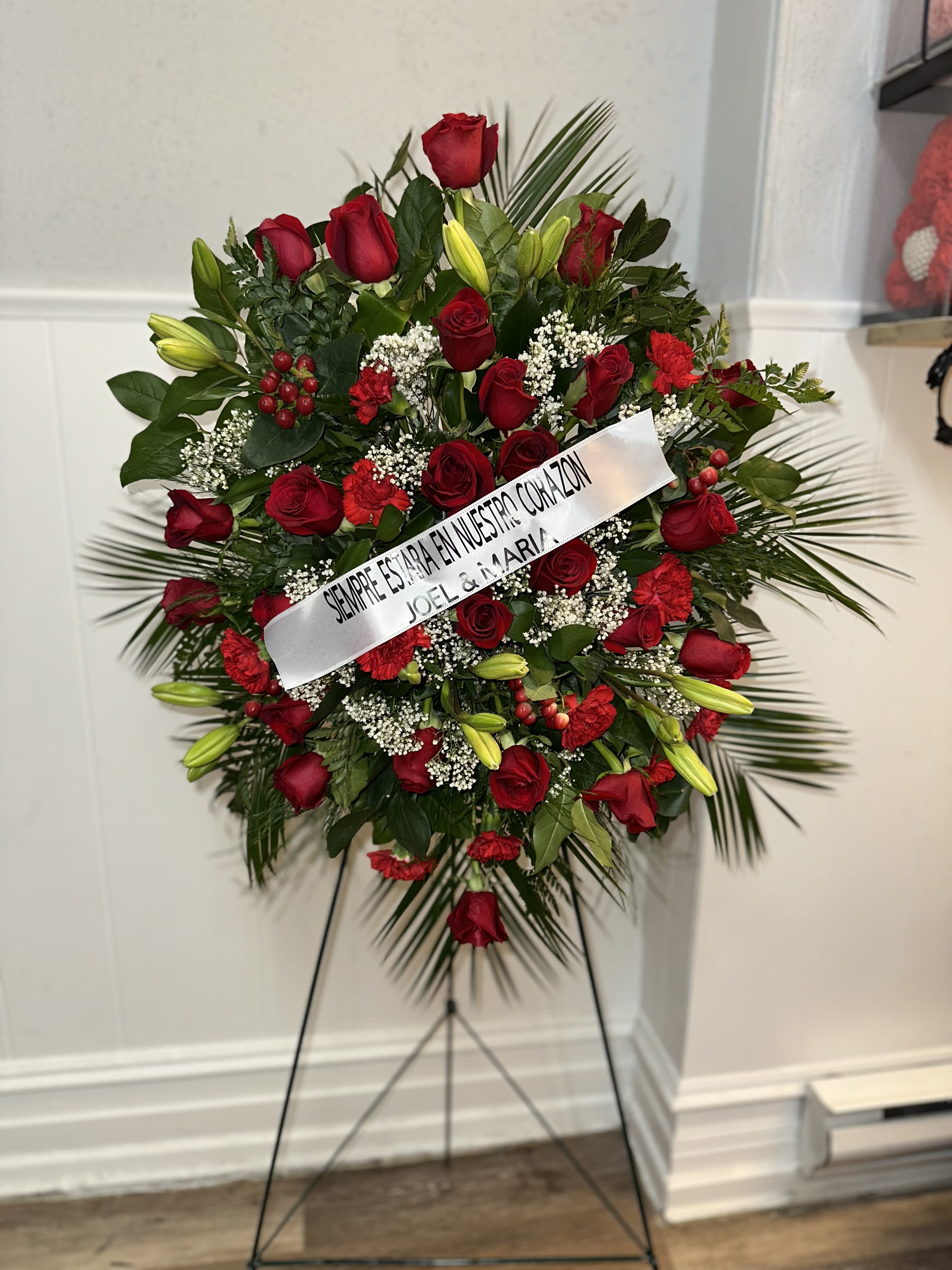 Standing floral spray of red roses and lilies with a white ribbon on an easel