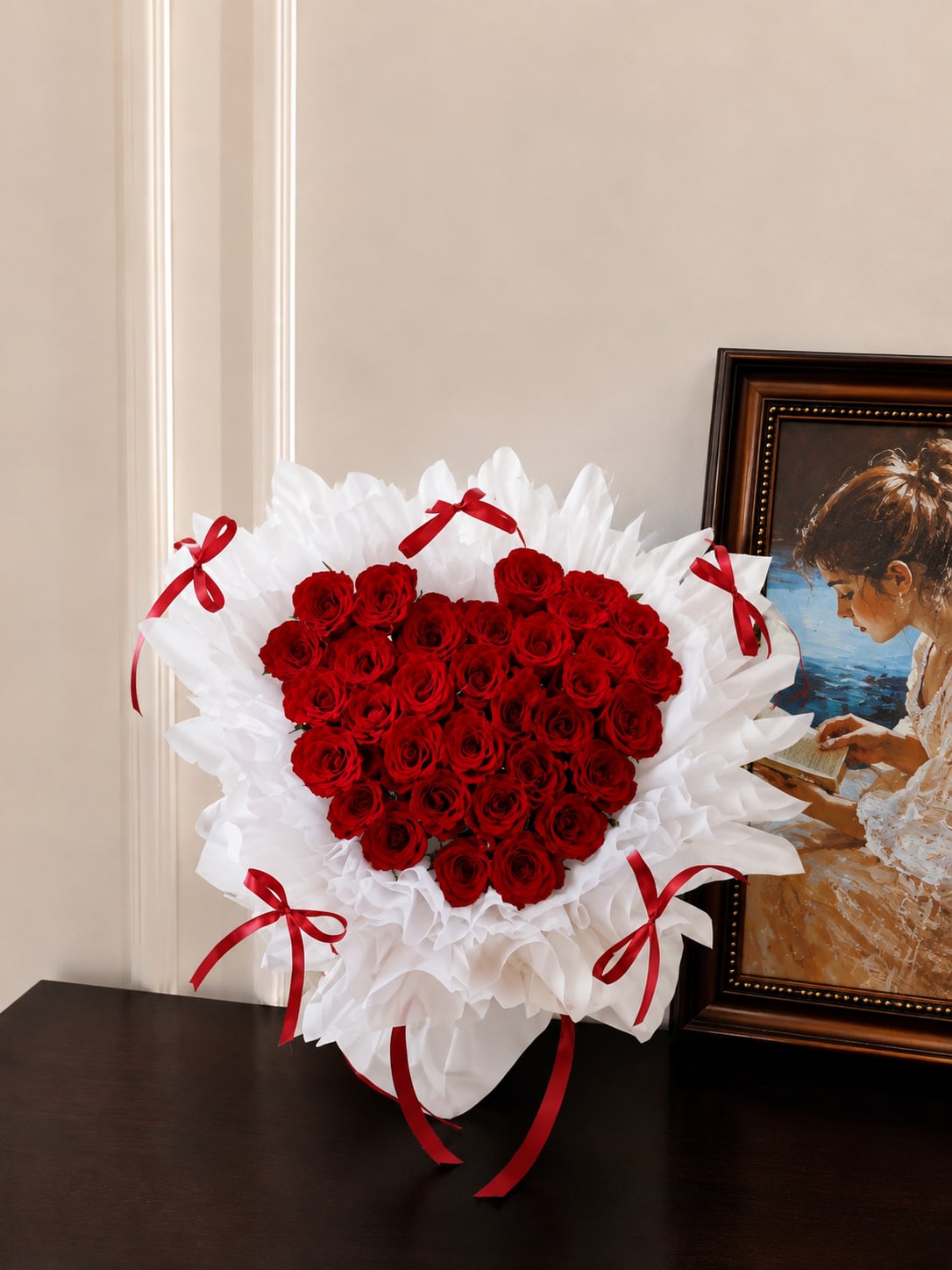 Heart-shaped bouquet of red roses with white wrapping and red ribbons