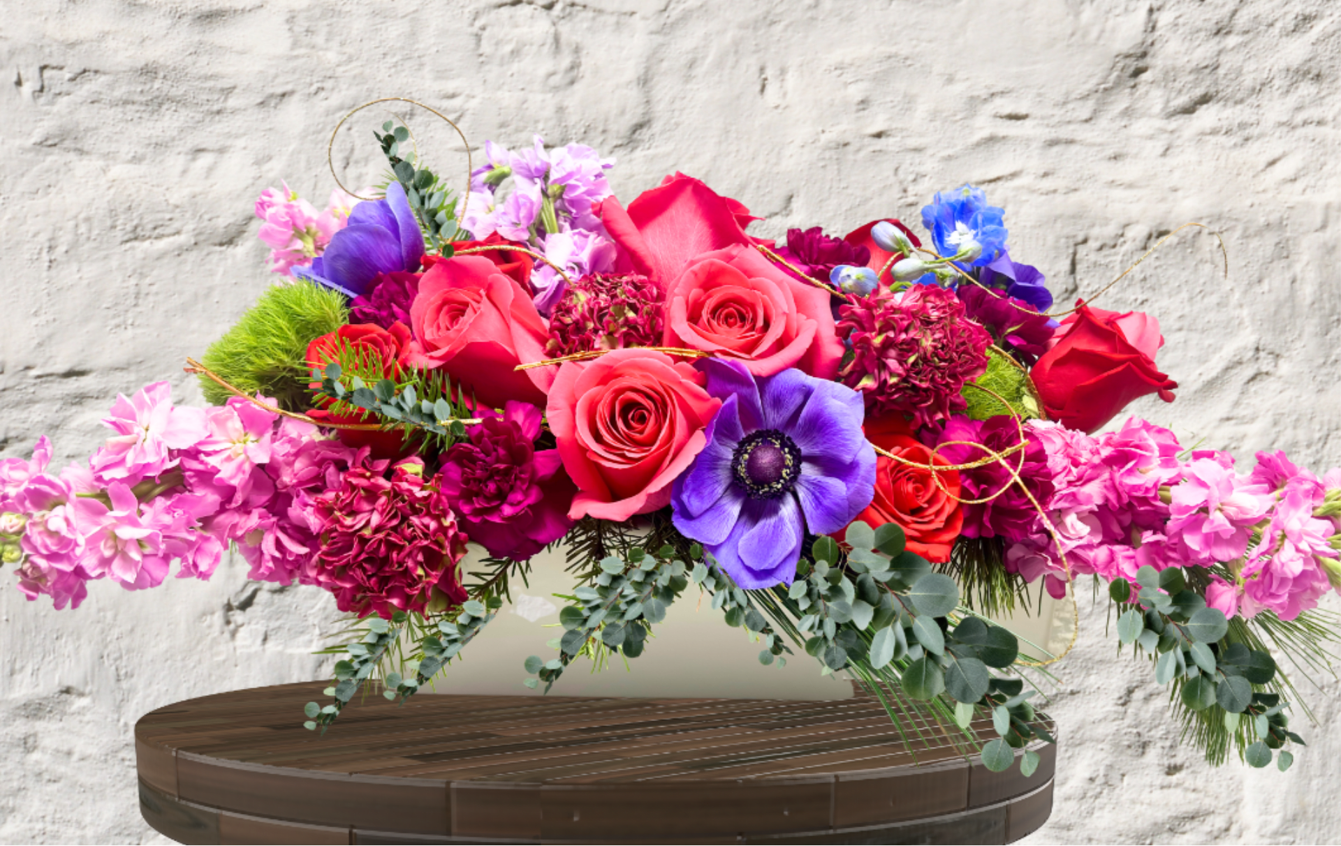 Regal Radiance - "Hand-crafted by accredited Master Florist Tricia Won (AIFD, EMC, IMF) using premium seasonal market blooms. No two arrangements are identical."  Bespoke Artistry. Jewel-Toned Splendor. Heirloom Elegance.  The Regal Radiance is a masterwork of texture and vibrant color, designed to serve as the crowning jewel of any setting. This elongated "Sovereign Statement" piece is a sprawling garden of high-contrast luxury, blending rich magentas and deep plums with striking pops of electric blue. It captures a sense of wild, sophisticated movement that flows effortlessly across a table or mantel.  The Design &amp; Florals This centerpiece is a premier example of our artisan craftsmanship, utilizing a low-profile silhouette that encourages conversation while commanding attention.  The Upscale Vessel: Presented in a sleek, elongated white ceramic planter. This clean, architectural foundation provides a crisp contrast to the overflowing jewel-toned blooms, ensuring the arrangement feels contemporary and high-end.  
