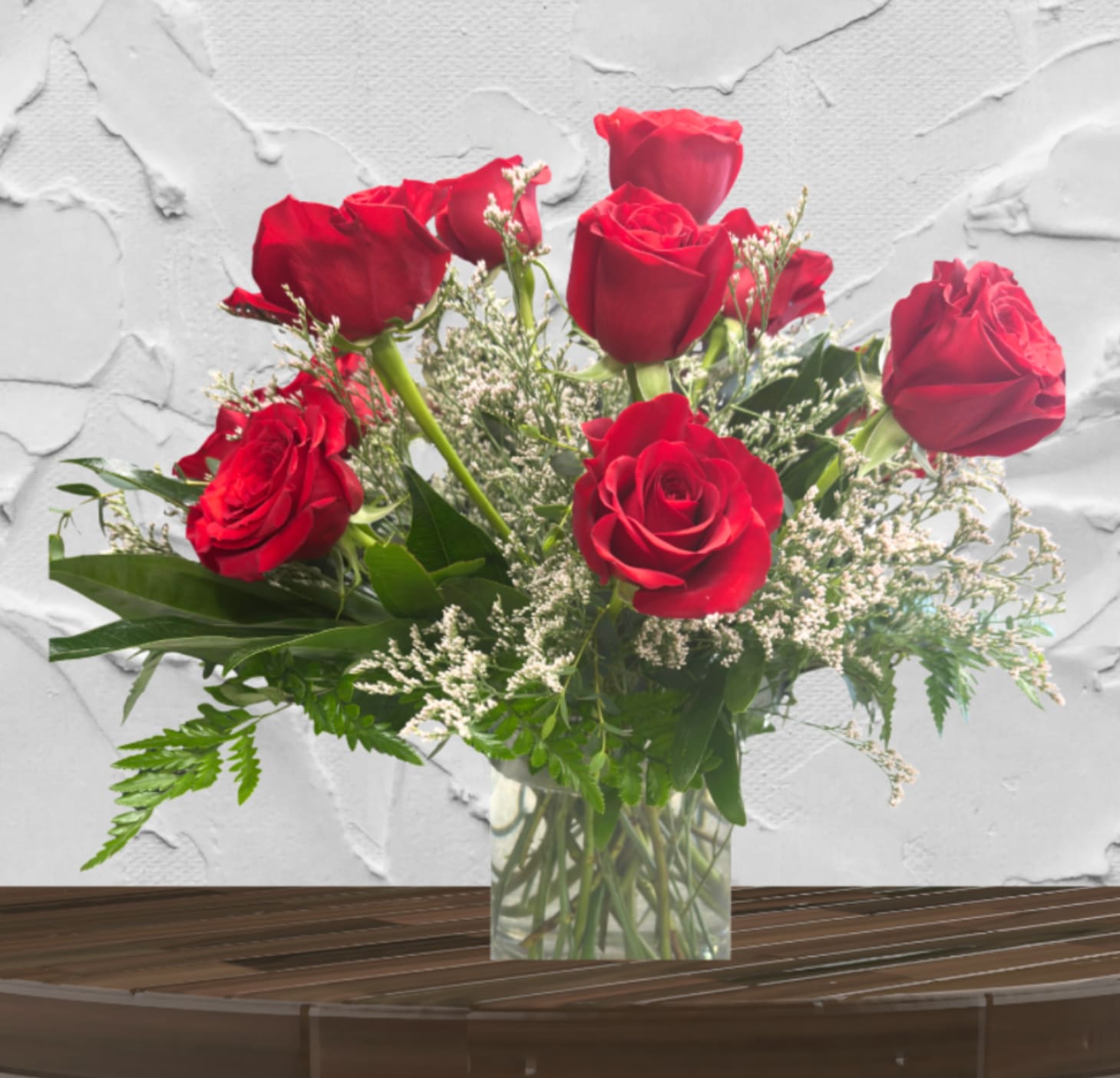 Red roses arranged in a clear glass vase with white filler flowers