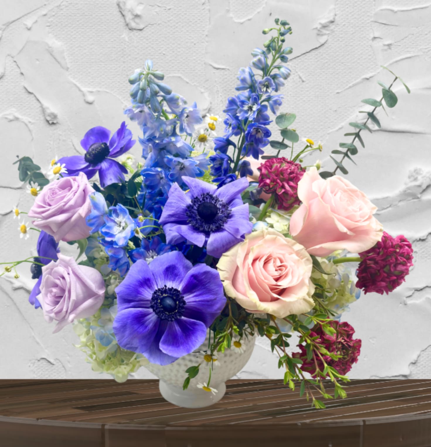 Twilight Serenade - "Hand-crafted by accredited Master Florist Tricia Won (AIFD, EMC, IMF) using premium seasonal market blooms. No two arrangements are identical."  Ethereal Blues. Romantic Pastels. Textured Sophistication.  The Twilight Serenade is a captivating study in color theory and garden-inspired movement. This arrangement strikes a perfect balance between cool, moody tones and soft, romantic warmth, making it a sophisticated choice for those who want a "soft but striking" aesthetic. It captures the fleeting magic of a garden at dusk, where vibrant indigos meet the gentle glow of late-afternoon light.  The Design &amp; Florals This arrangement is a premier example of our "Bespoke Choice" expertise, blending high-end structure with whimsical, airy details.  Premium Blooms: The focal point features dramatic, premium seasonal blooms in a rich palette of deep purple lush lavender and pink tones.   The Upscale Vessel: Set in a classic, white footed ceramic compote with a subtle "honeycomb" or "beaded" texture. This clean, bright vessel allows the complex colors of the blooms to take center stage and serves as a versatile, high-end piece for any home interior.  
