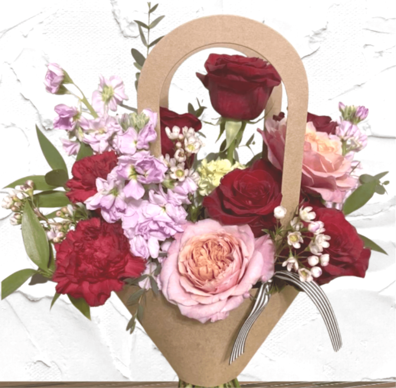 Mixed bouquet of red, pink, and lavender flowers in a kraft paper wrap