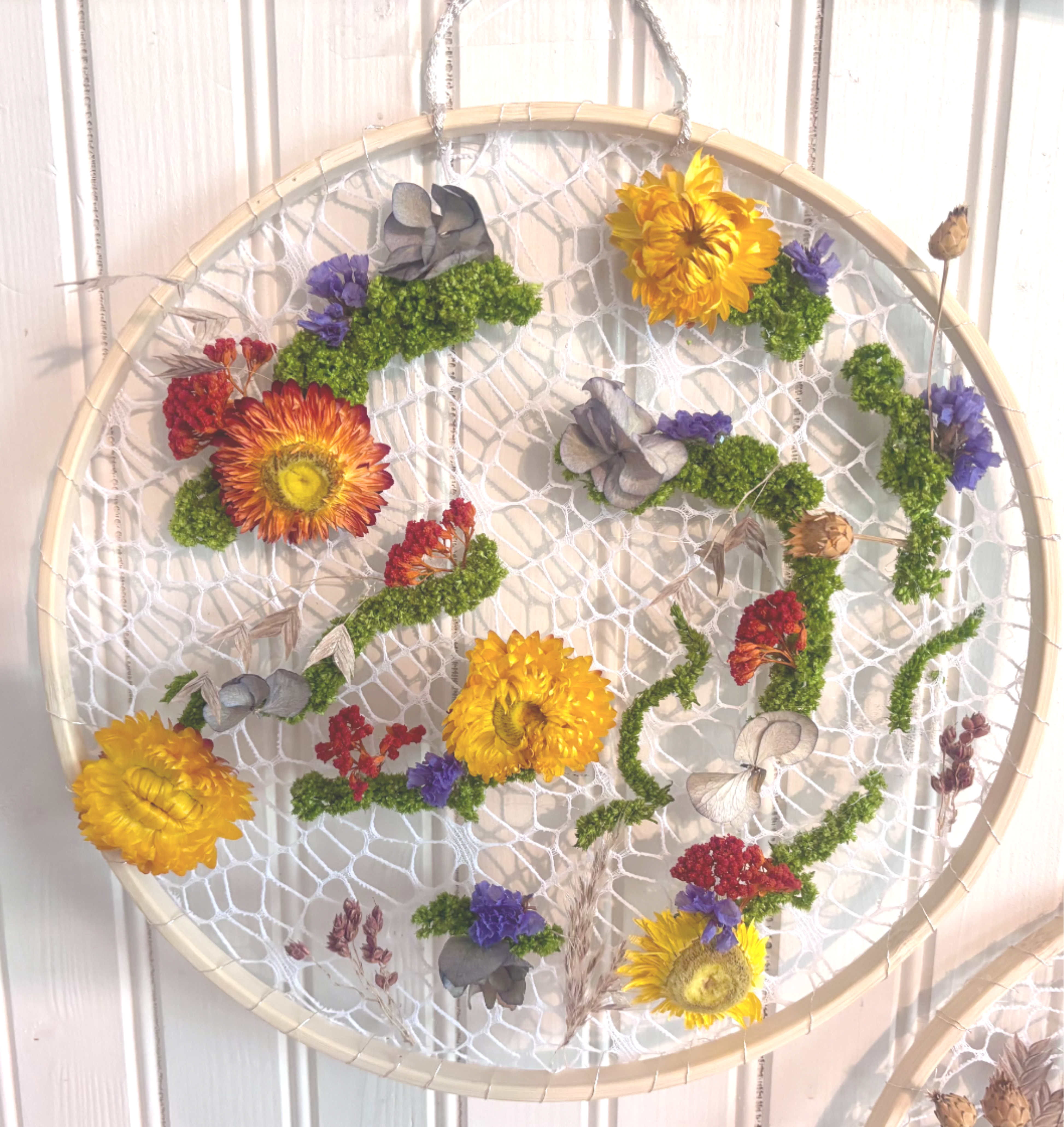 Wildflower Tapestry Hoop - A modern take on traditional fiber art, this handcrafted piece weaves real preserved botanicals into intricate lace netting like a living wall tapestry. Rich strawflowers, moody hydrangeas, textured moss, and delicate dried blooms form an organic floral tapestry set within a natural wooden hoop. Designed to bring textural warmth and rich botanical color to your space, this everlasting piece hangs like a delicate textile masterpiece.