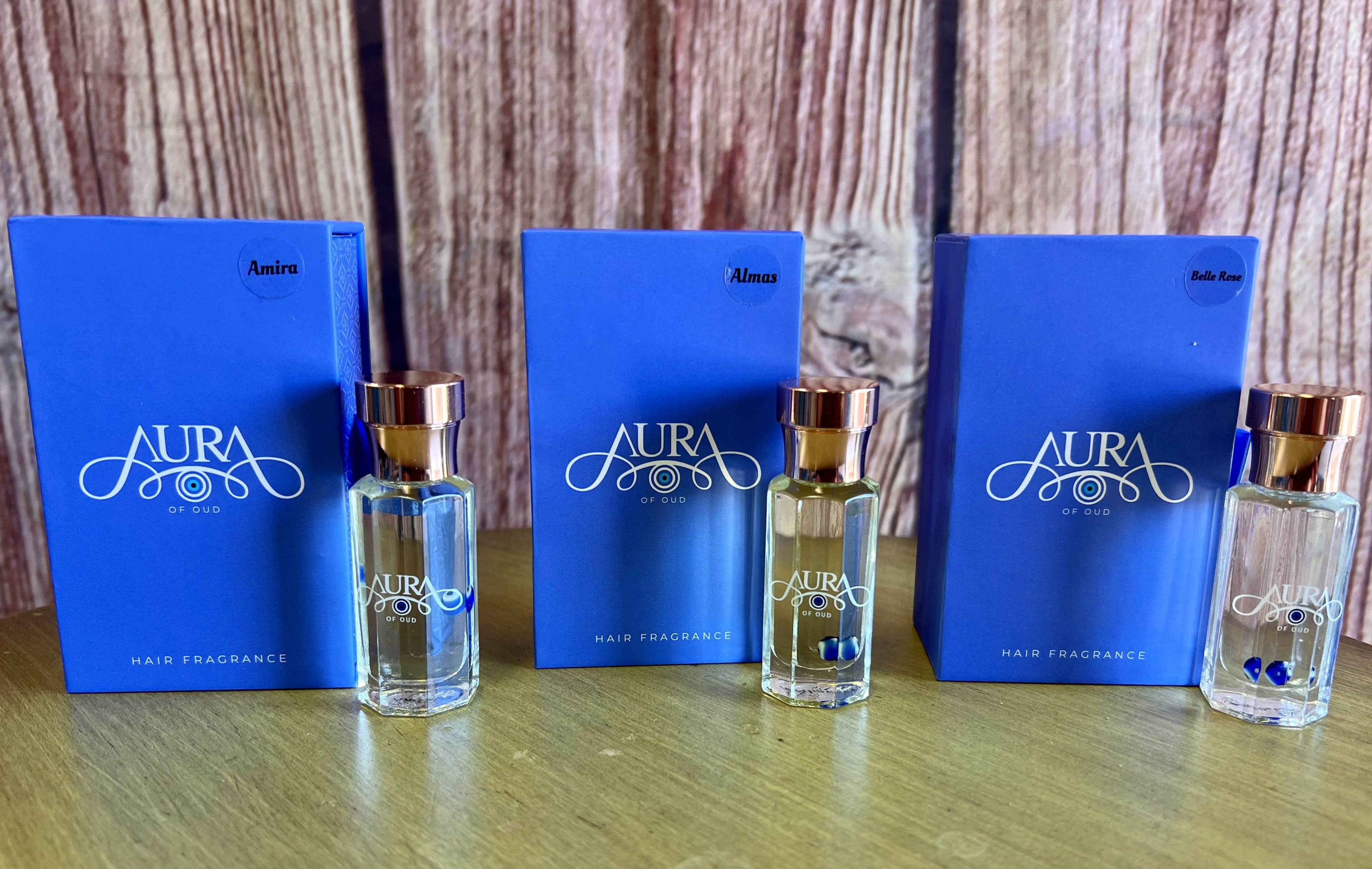 Three blue hair fragrance boxes with matching glass bottles on a wooden surface