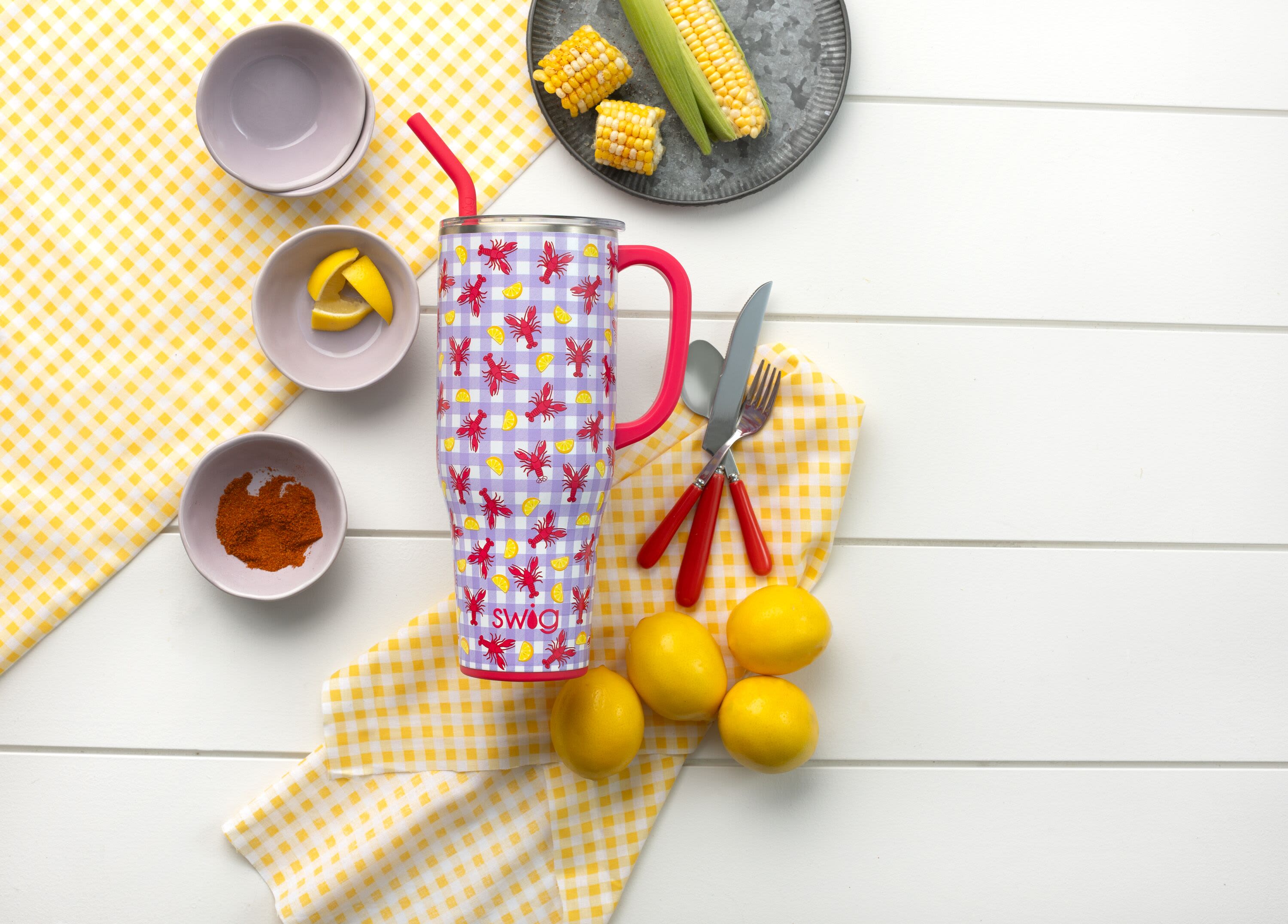 Patterned insulated tumbler with straw surrounded by lemons and picnic dishes