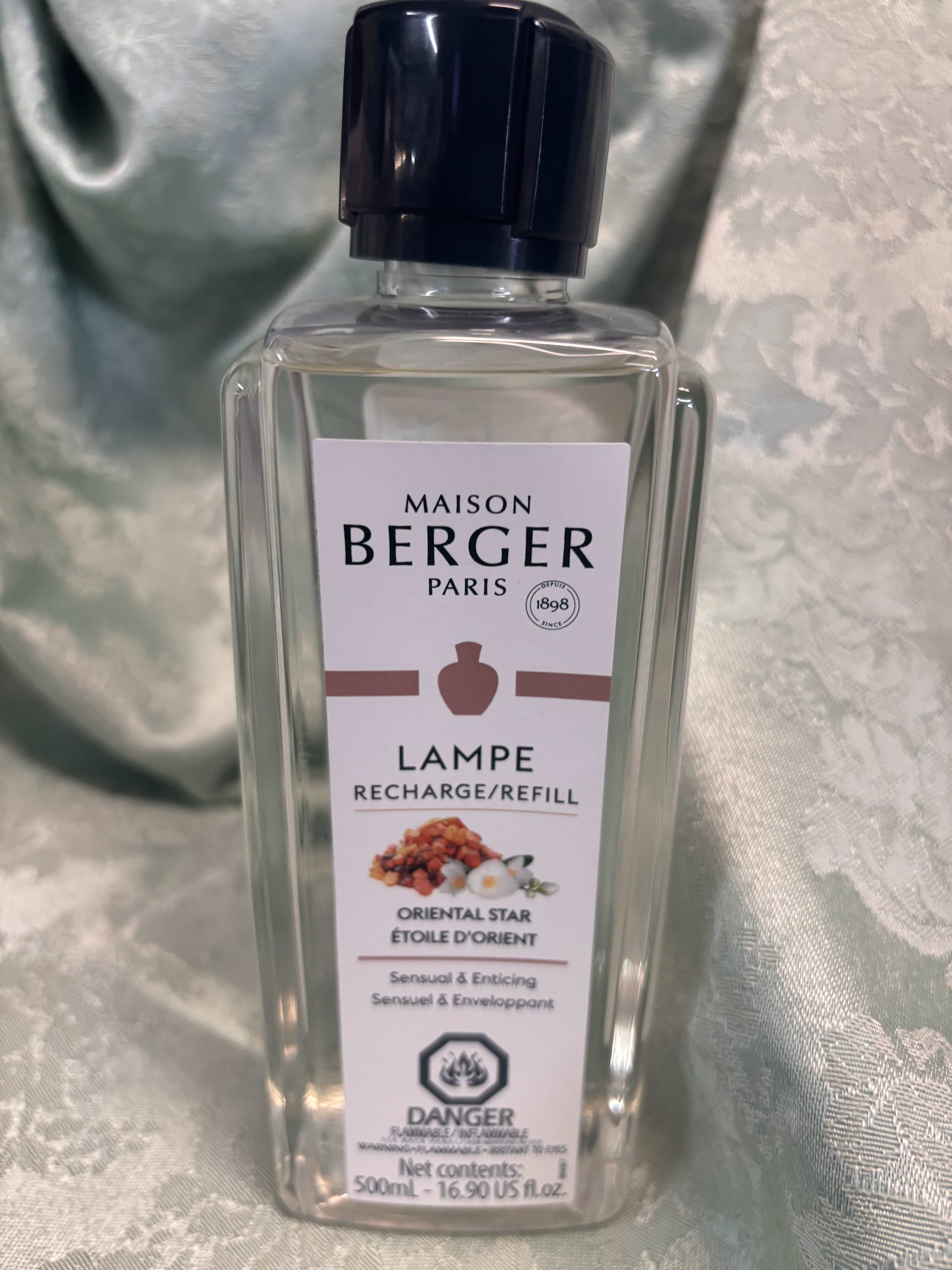 Clear Maison Berger refill bottle with a black cap on a satin background