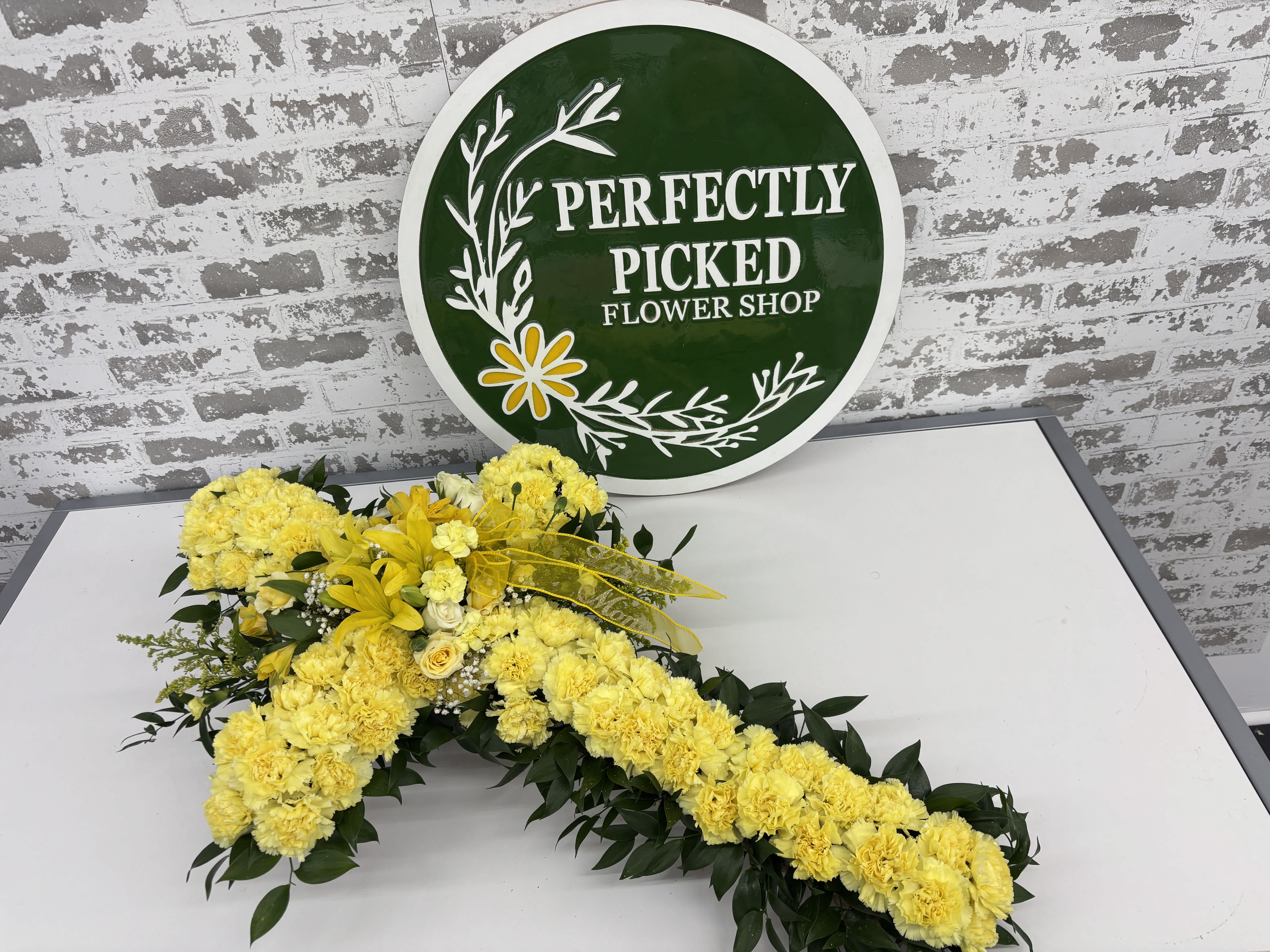 Yellow floral cross with dark green foliage on a table
